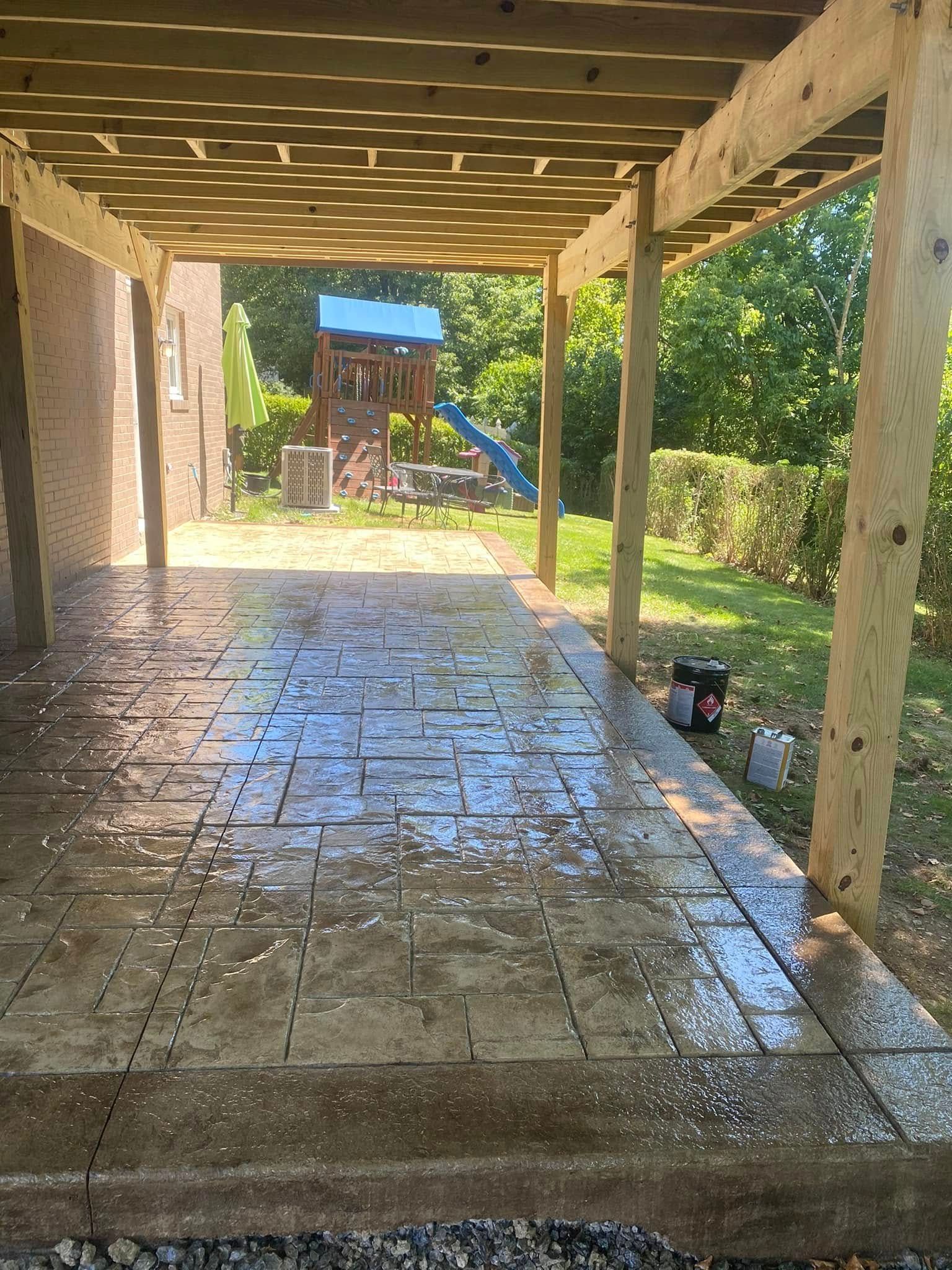 Covered patio with wet tiled floor, wooden posts, and a backyard playset in the distance.