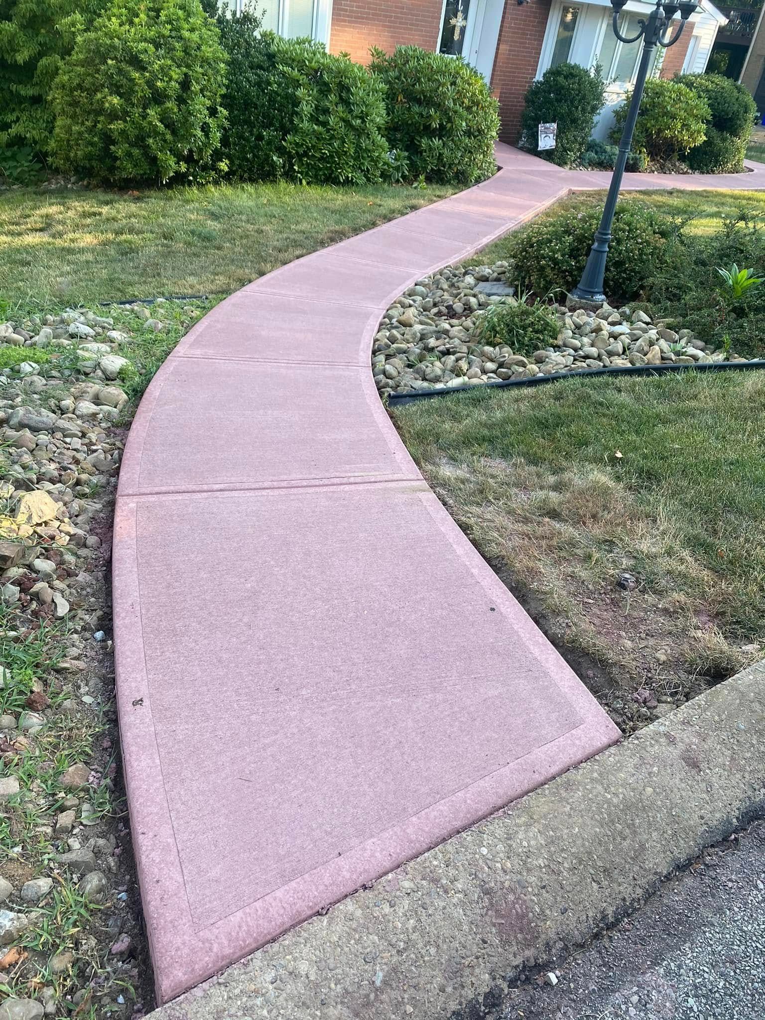 Curved pink sidewalk through a landscaped garden with shrubs and a lamp post
