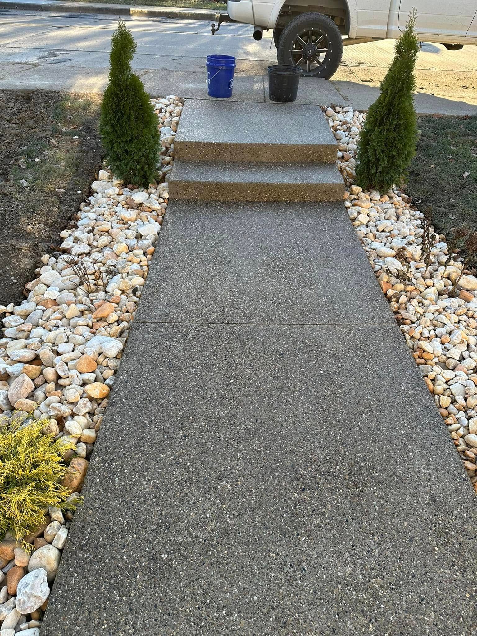 Front walkway with gravel border, three steps, and small evergreen shrubs leading to a driveway.