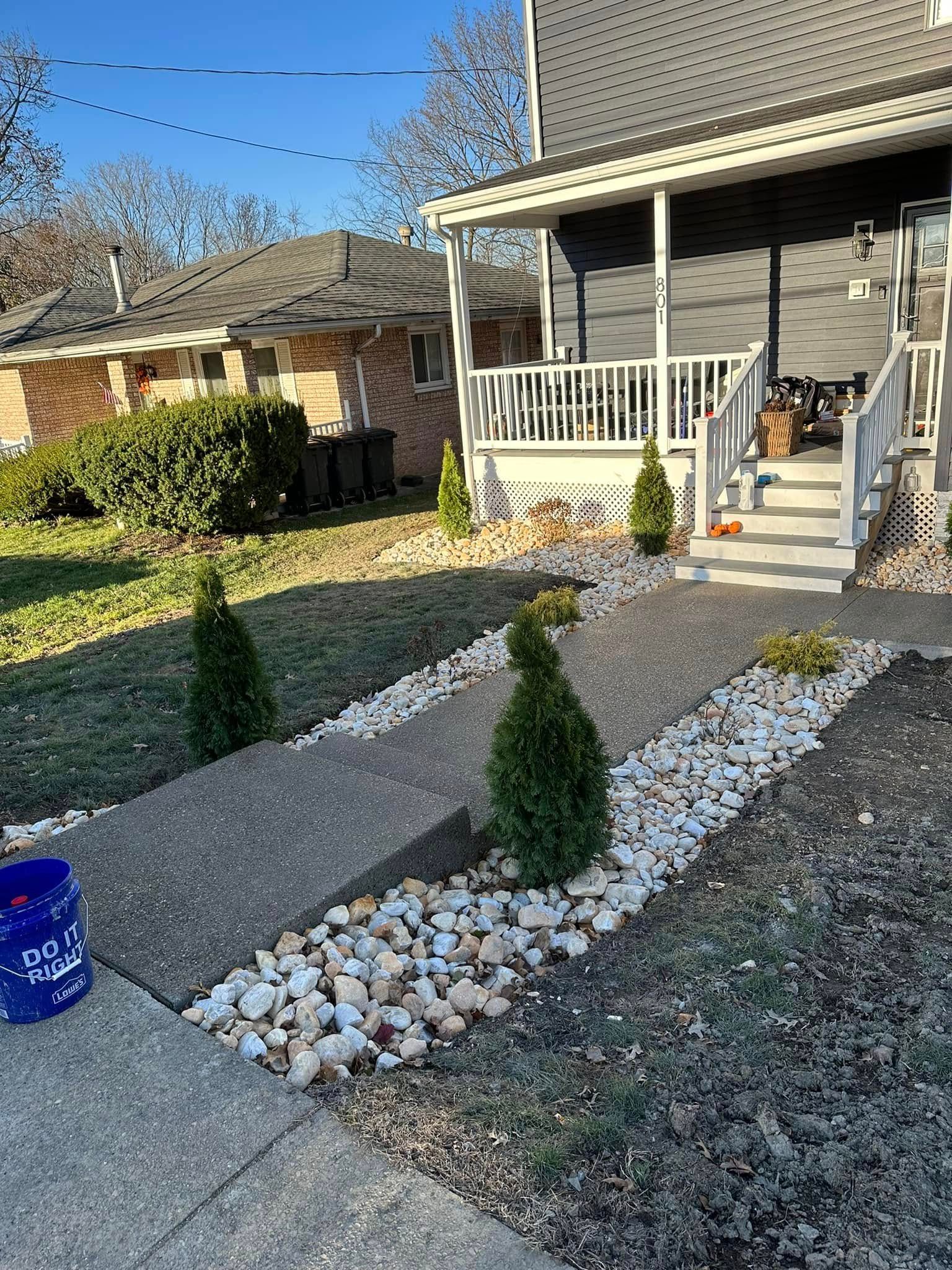 Front yard with gravel paths, small evergreen shrubs, and a house porch with white railings and steps.