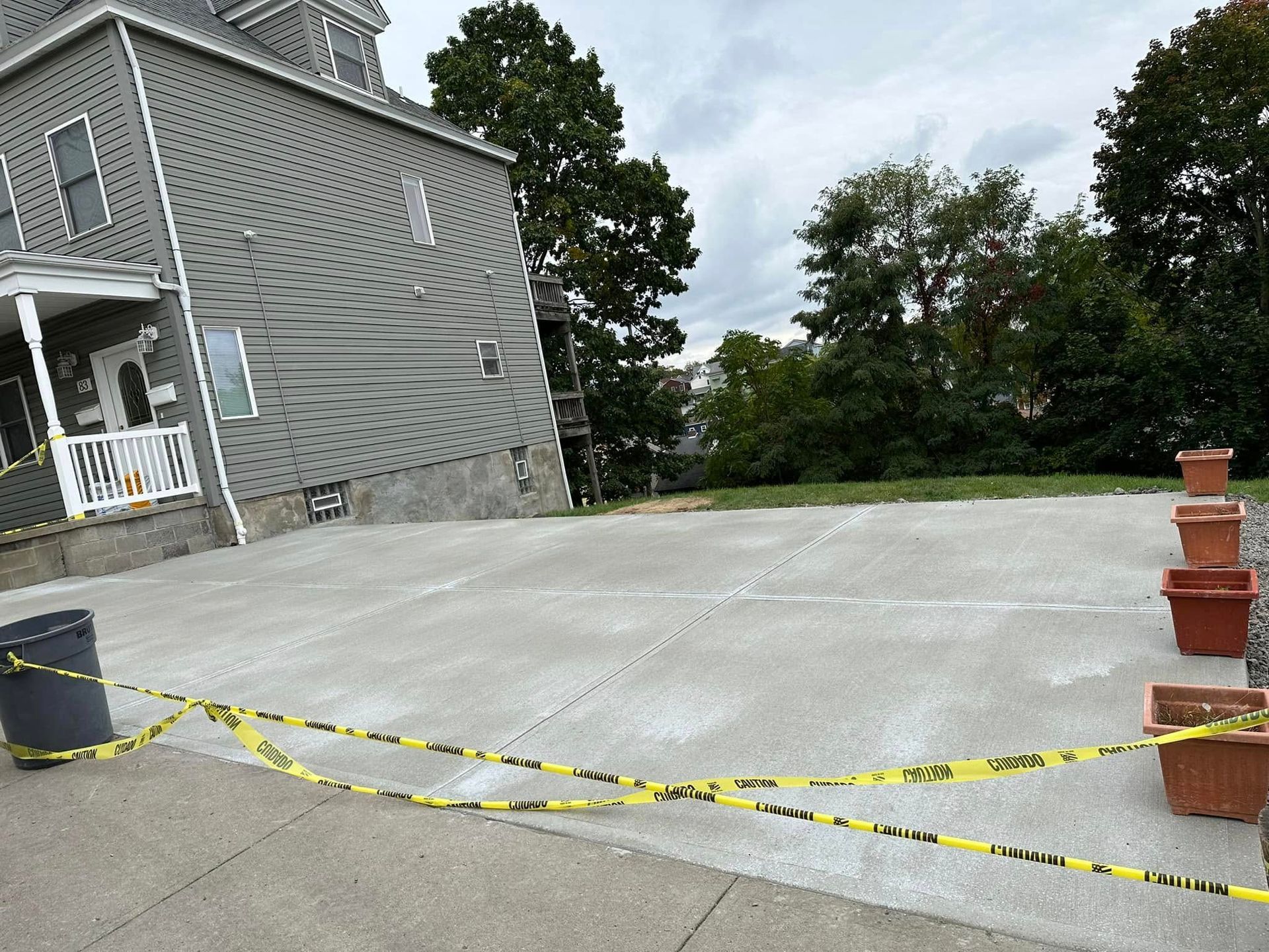 Concrete driveway blocked by yellow caution tape beside a gray house and trees