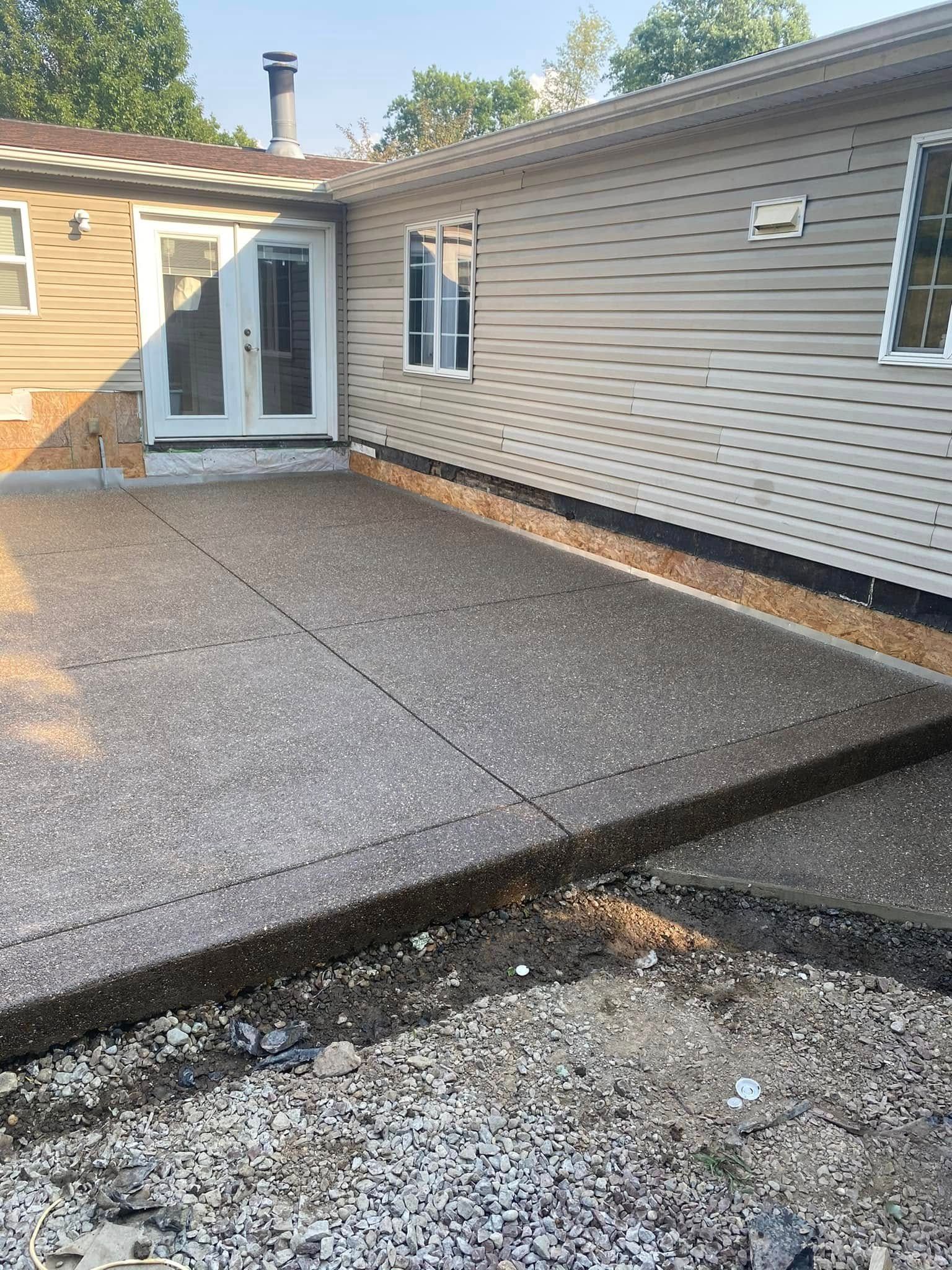 Backyard patio with gray pavers beside a house, leading to a white door and siding.