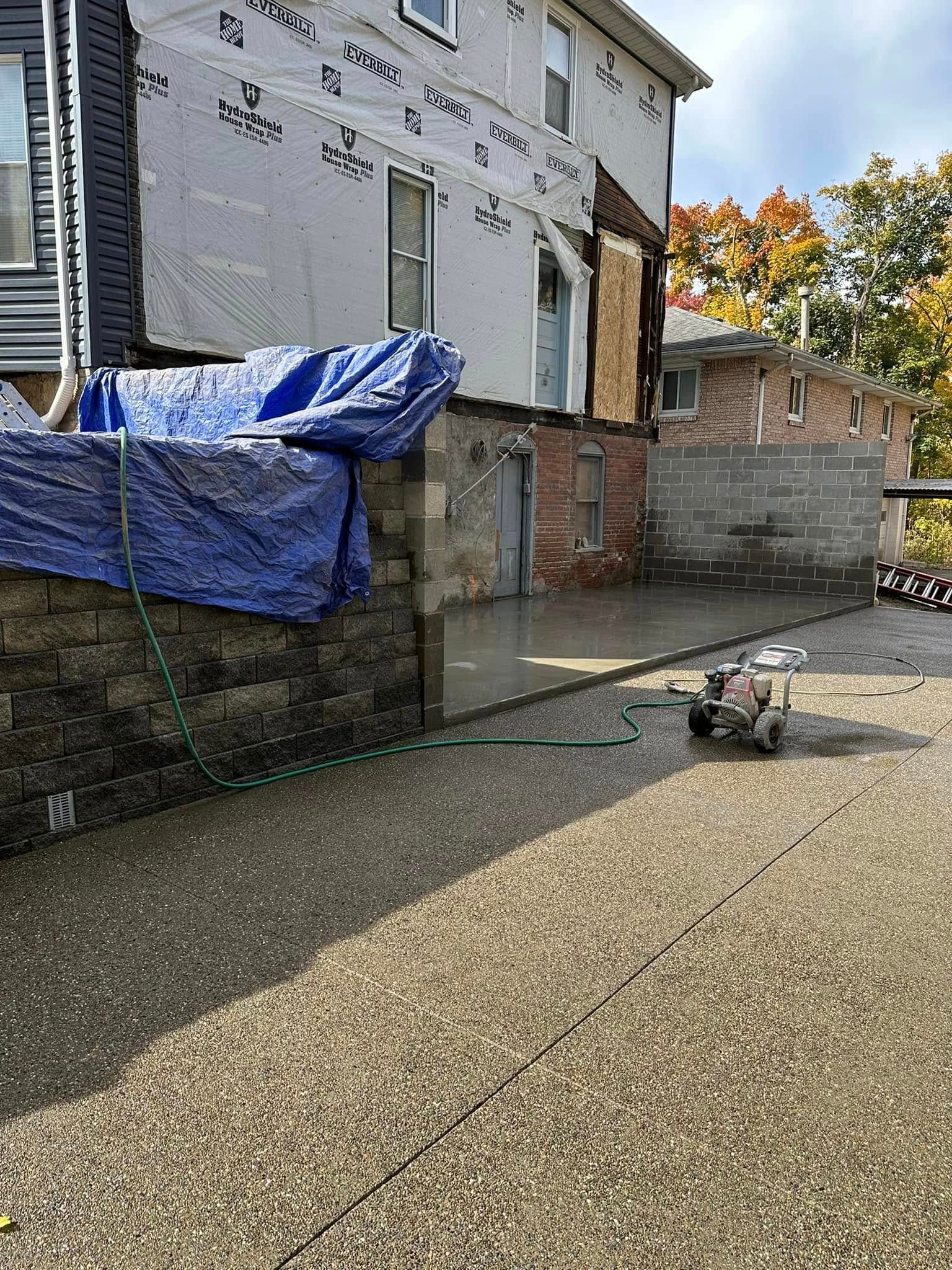 A small dog on a leash stands on a paved driveway beside a house under repair.
