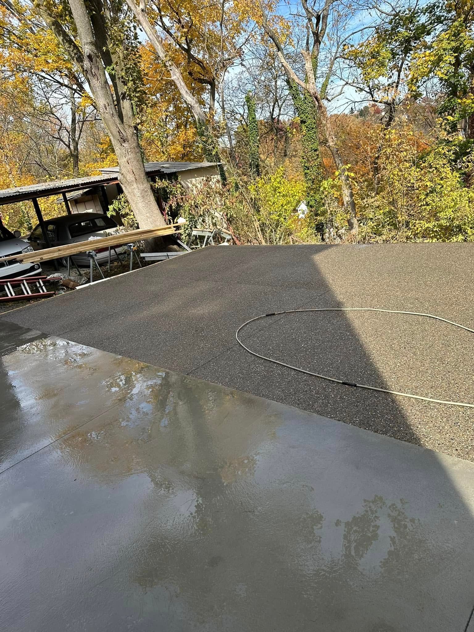 Wet concrete patio beside a wooden deck, with autumn trees and bushes in the background.