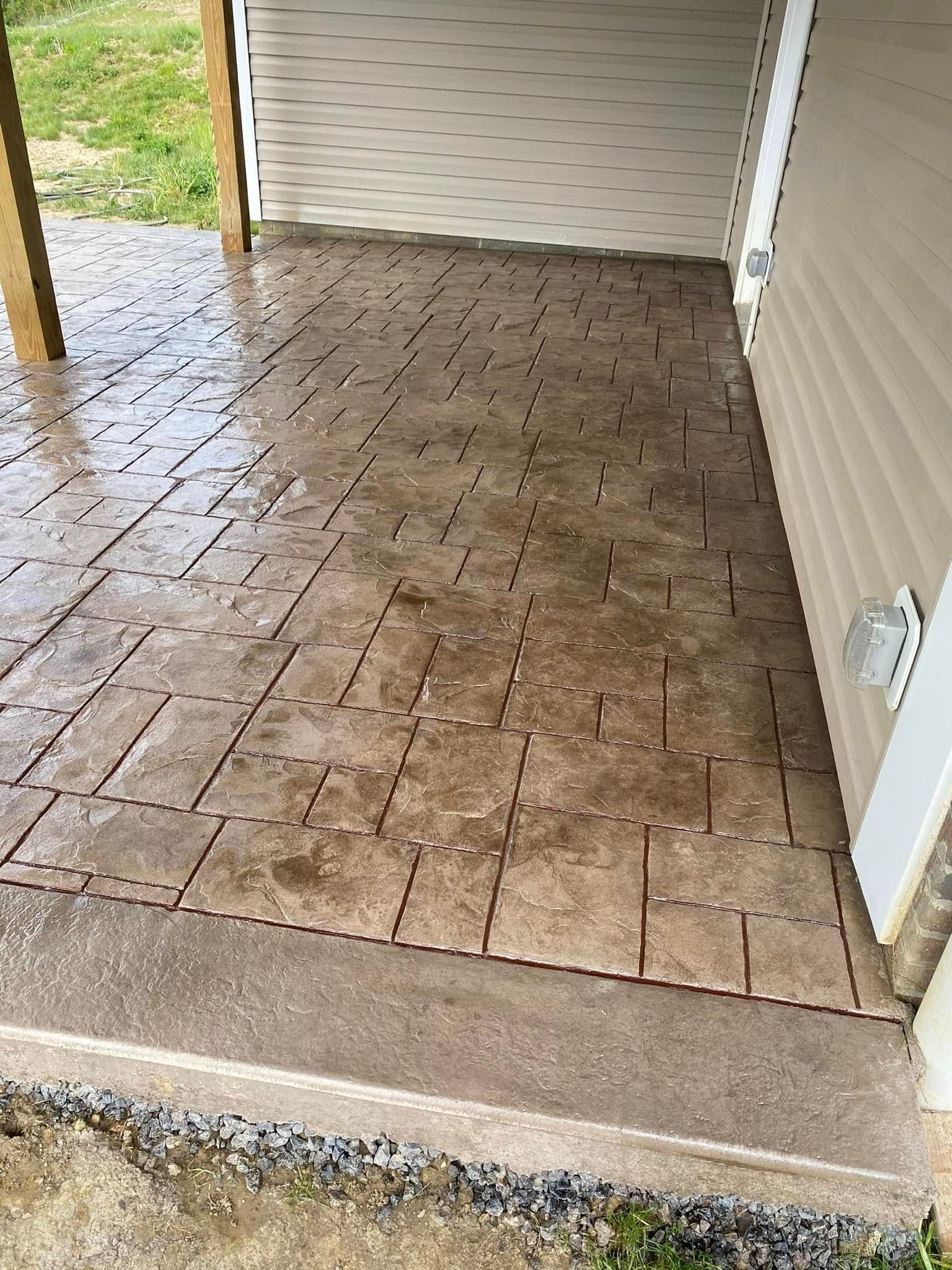 Covered brick patio beside a garage, with a step and a white object near the right wall.