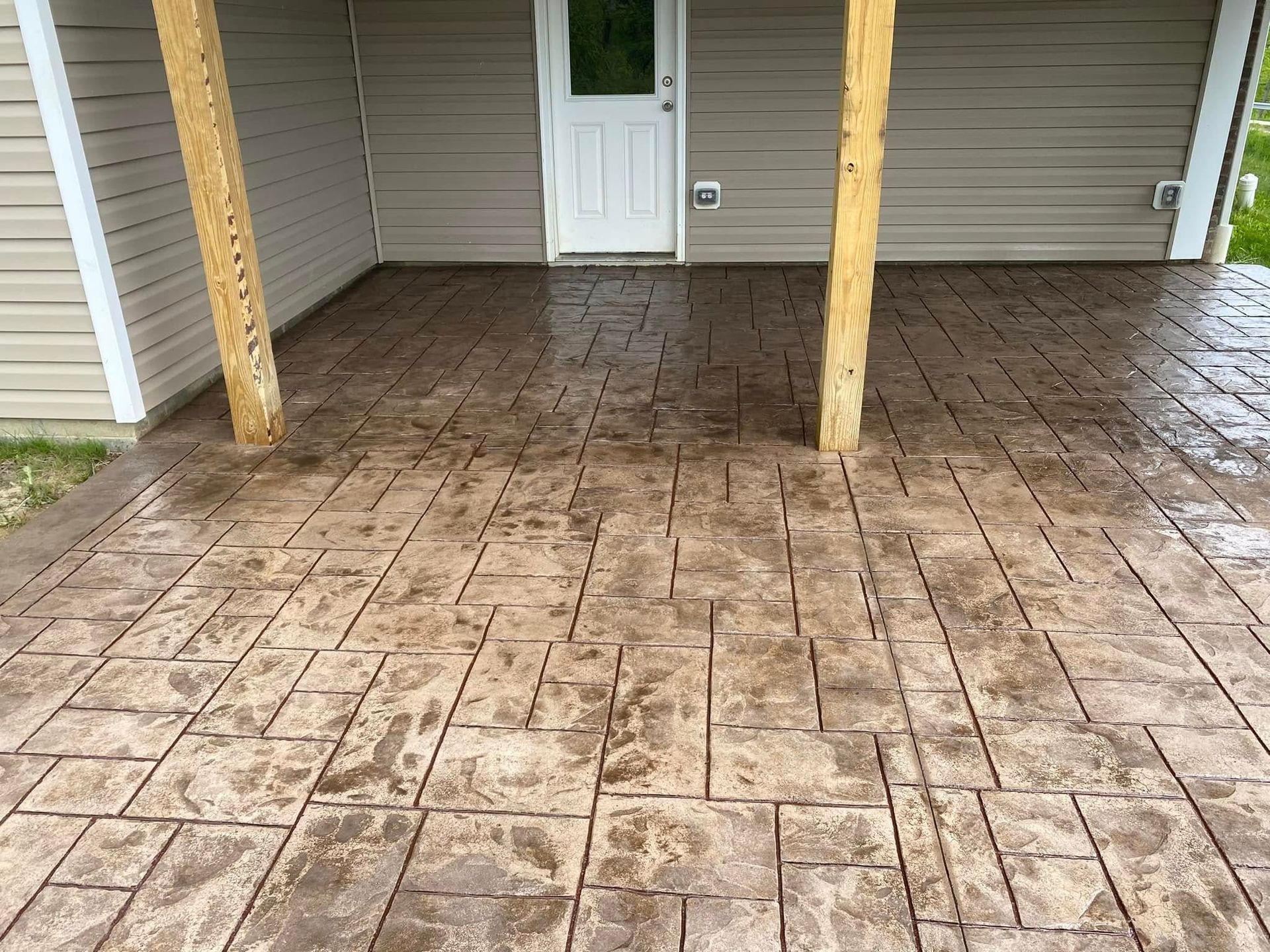 Covered porch with wet stamped concrete floor, wooden posts, and a white door on a gray house