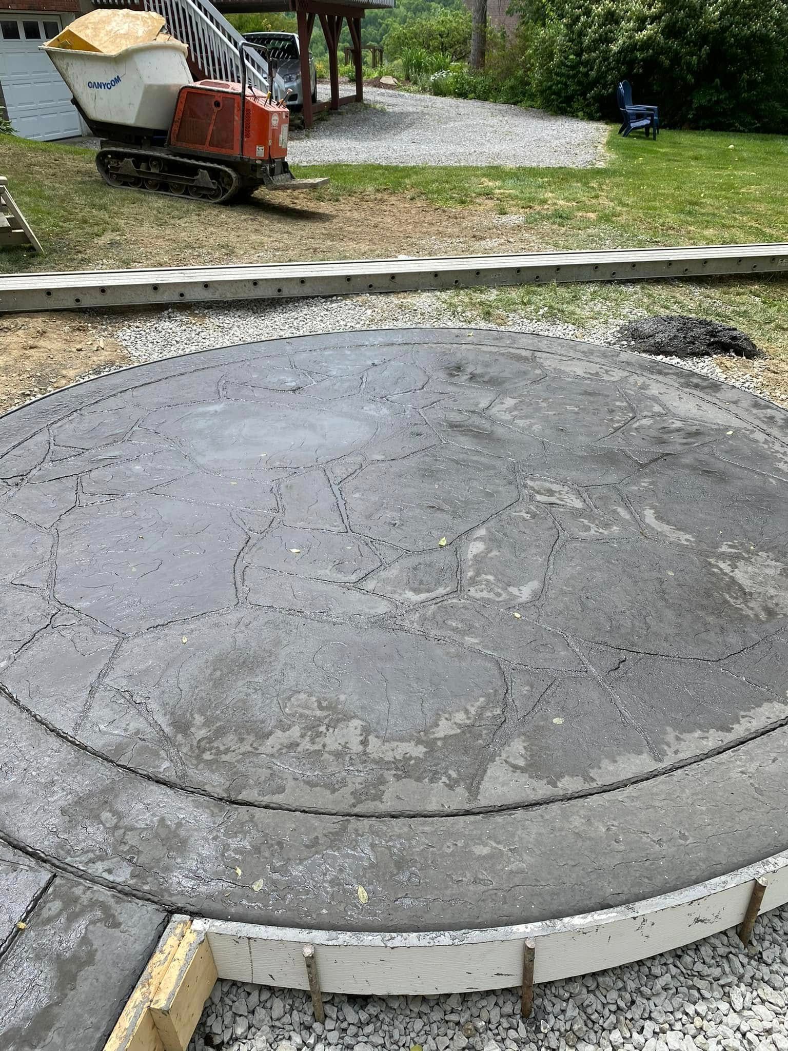 Concrete circular patio slab under construction with a wheelbarrow and gravel in the background