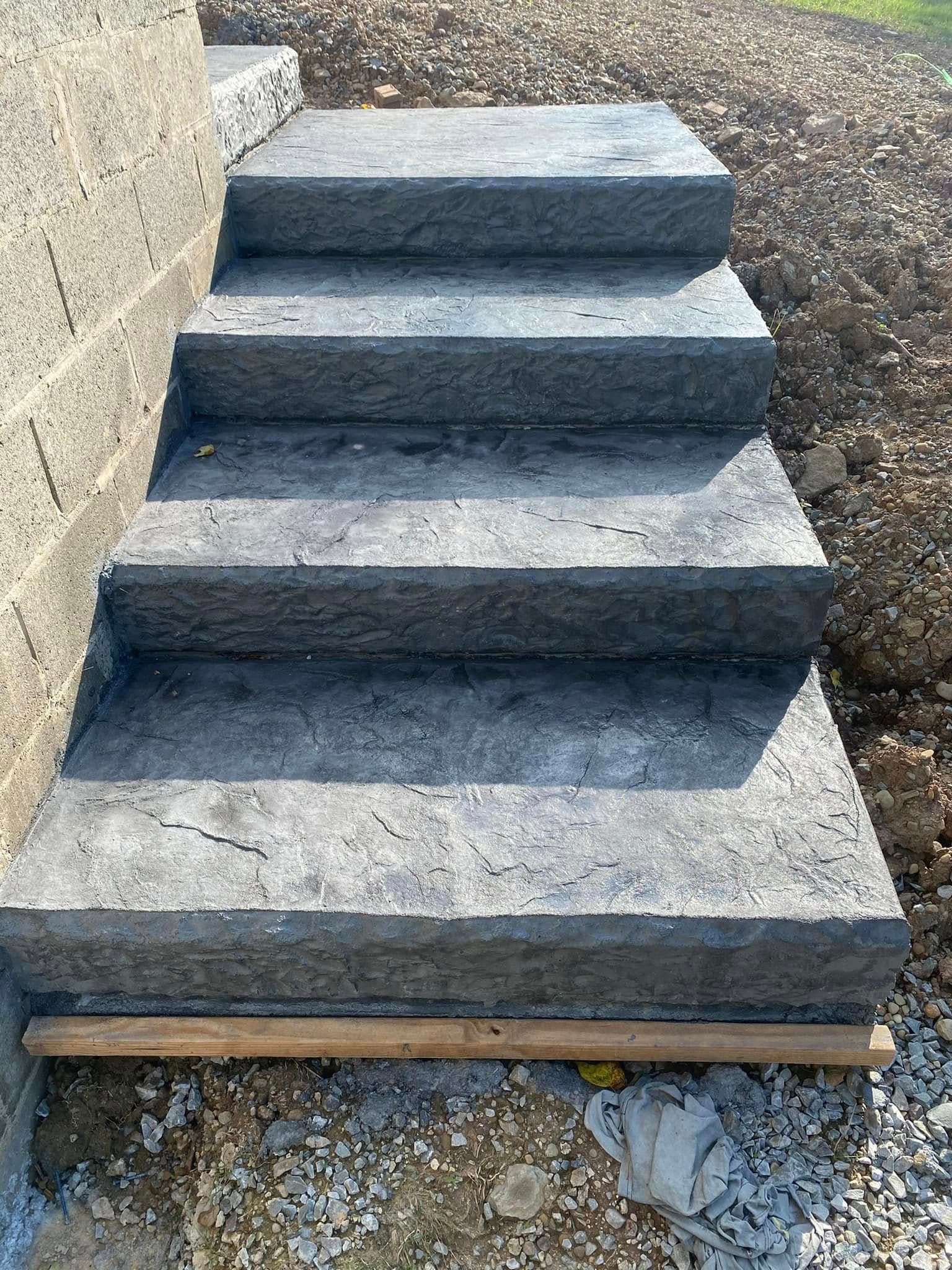 Stone steps on a dirt slope beside a retaining wall, viewed from the front.