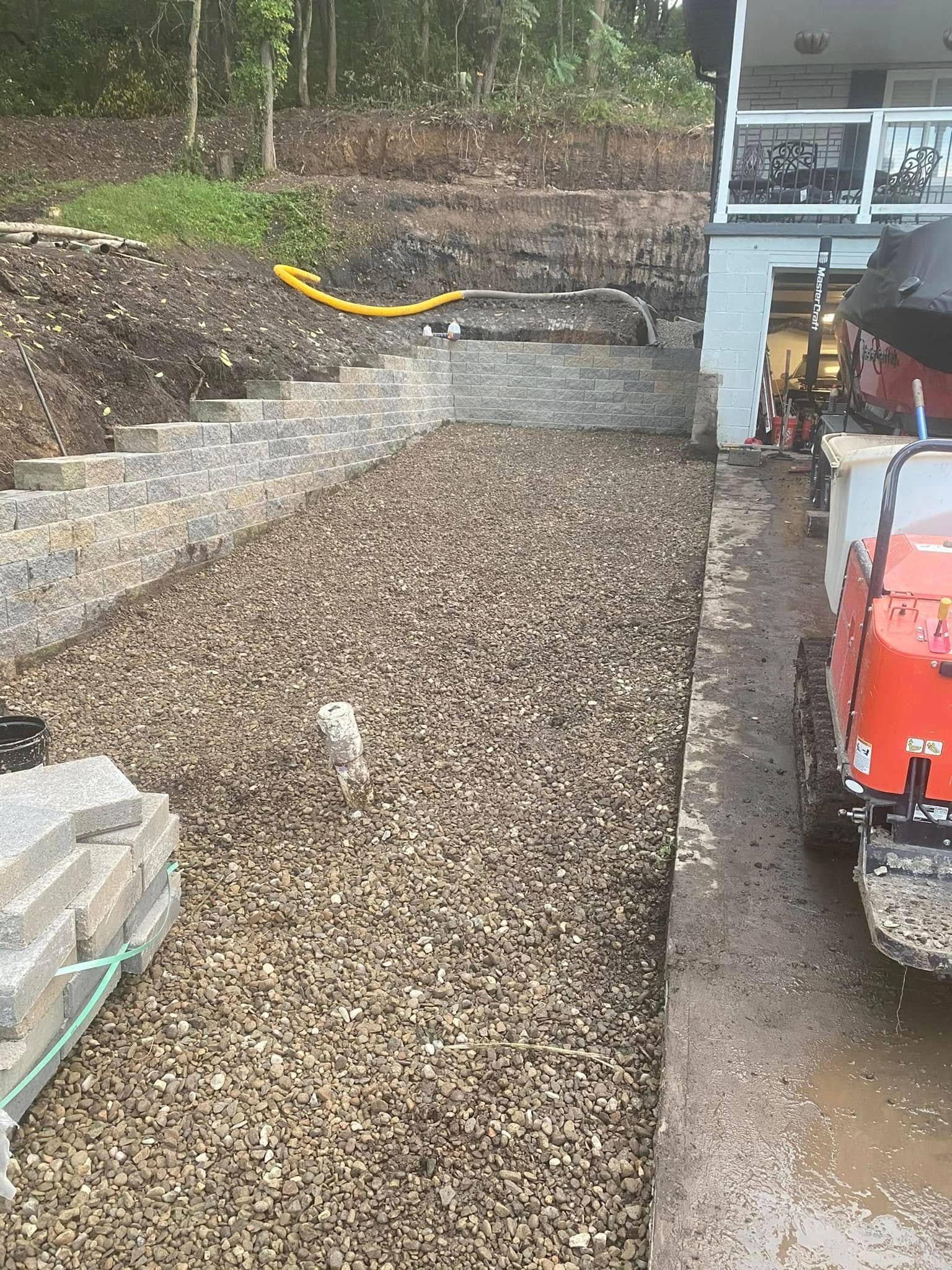 Gravel driveway under construction beside a house, with a red machine and landscaping materials.
