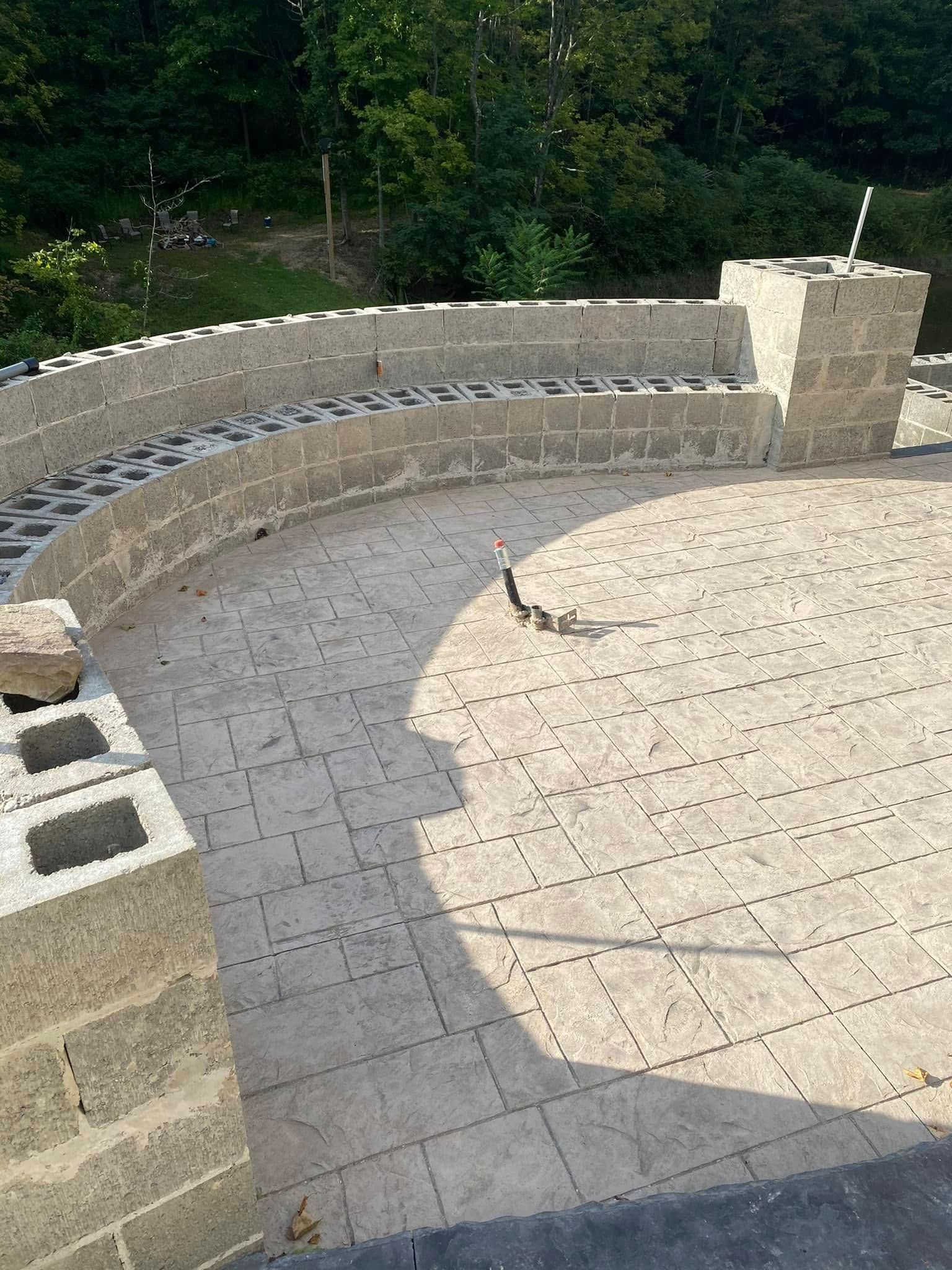Curved stone patio with a retaining wall and steps beside a wooded area