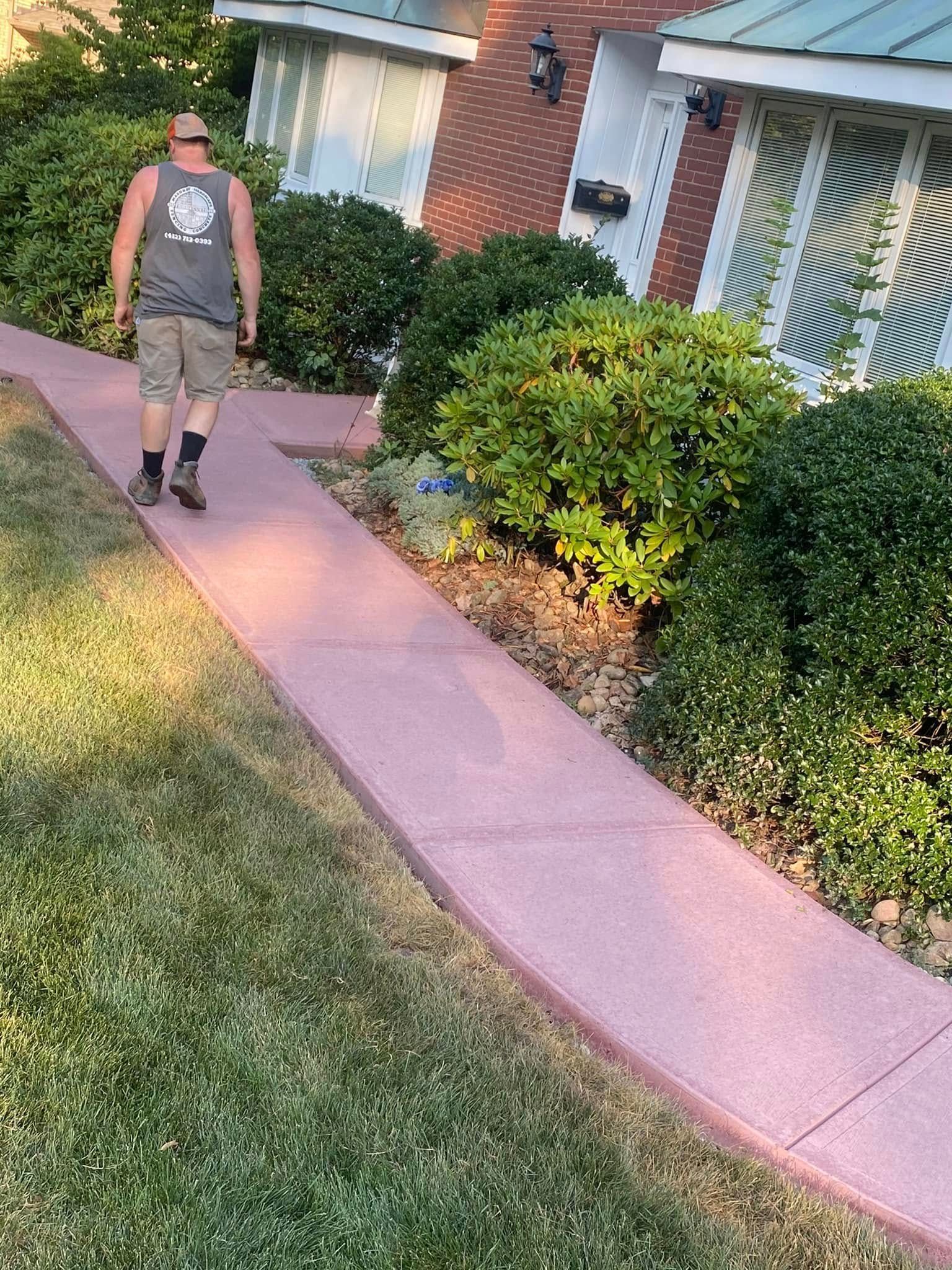 Person walking on a pink sidewalk beside a brick house and green lawn.