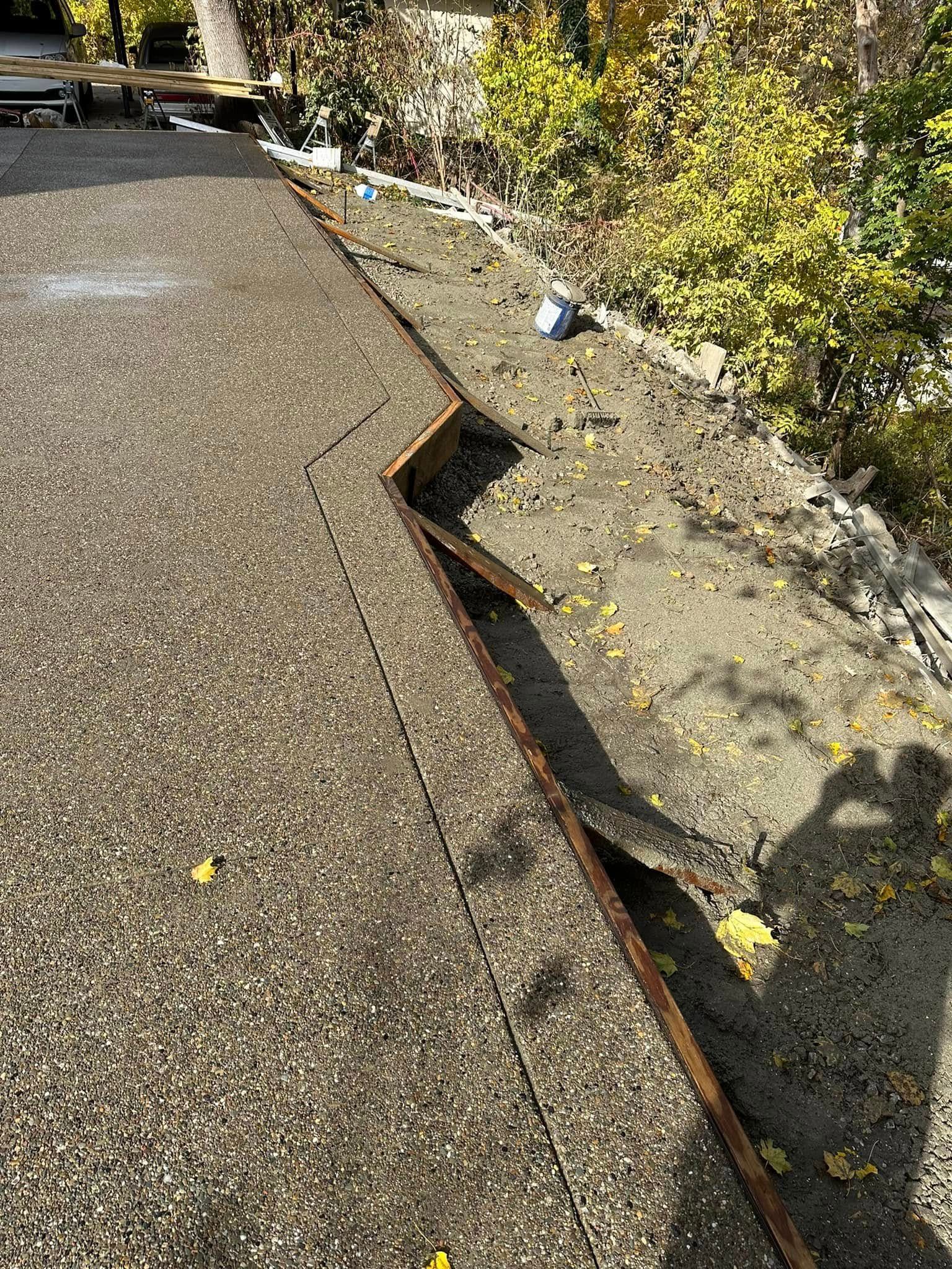 Broken sidewalk edge with a large gap beside a gravel path and overgrown bushes