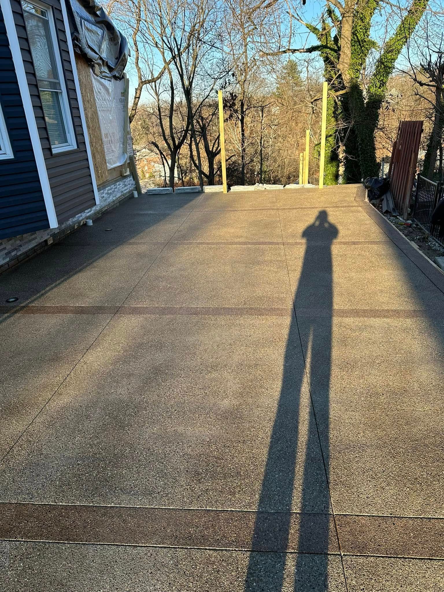 Long shadow on a sunlit concrete driveway beside a house and trees