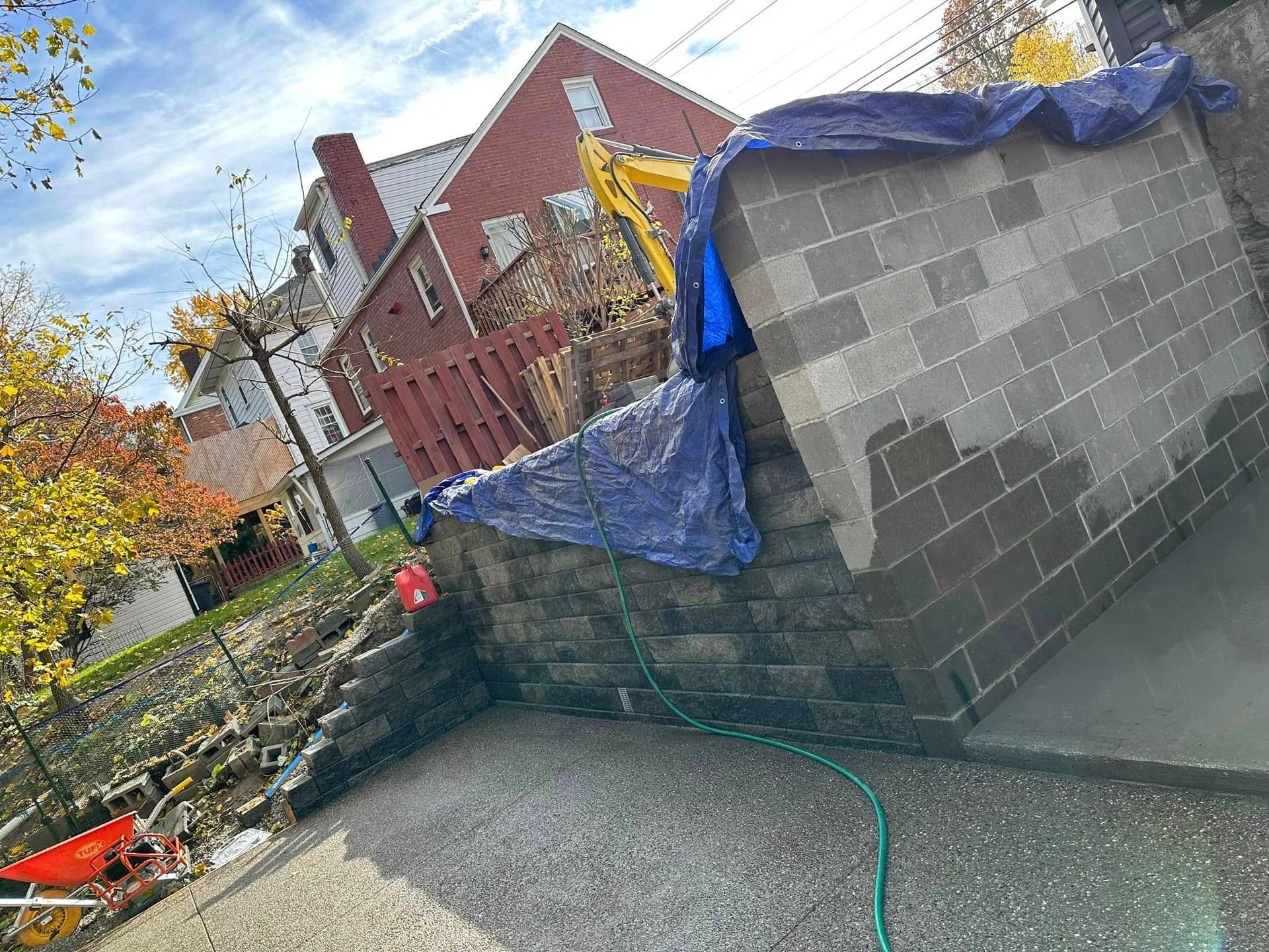 Backyard with a cinderblock shed covered in blue tarp, gravel ground, and autumn trees near a brick house