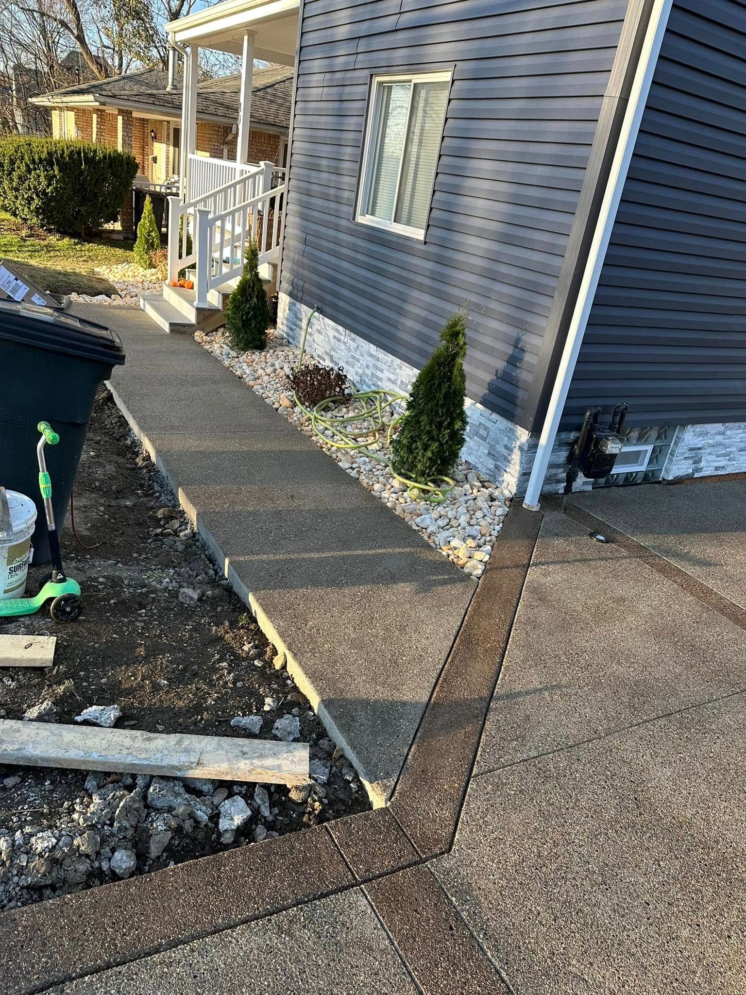 Side yard walkway beside a blue house, with pavers, small shrubs, and fresh gravel edging.