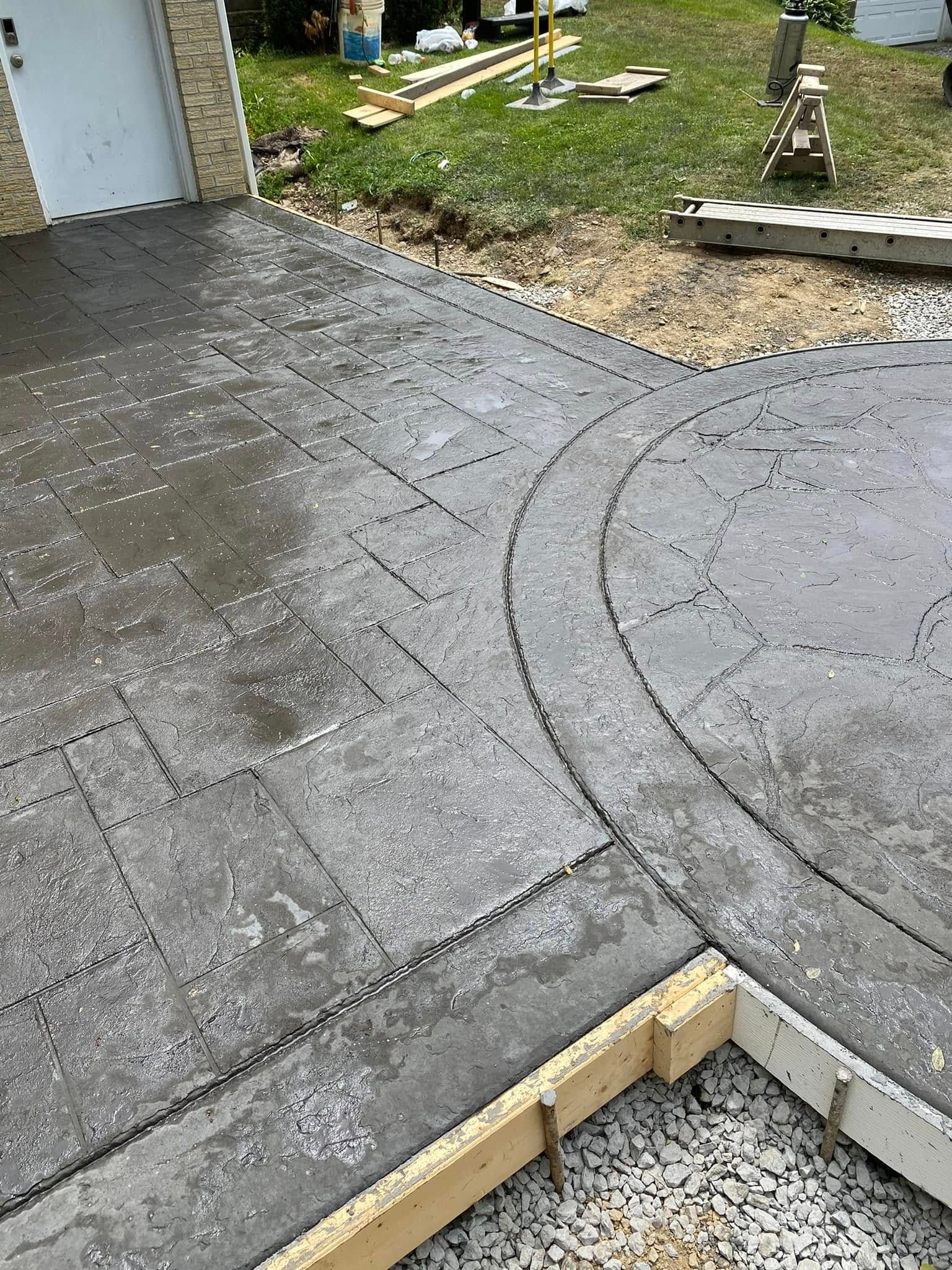 Freshly laid gray concrete paver patio beside a gravel yard and wooden edging