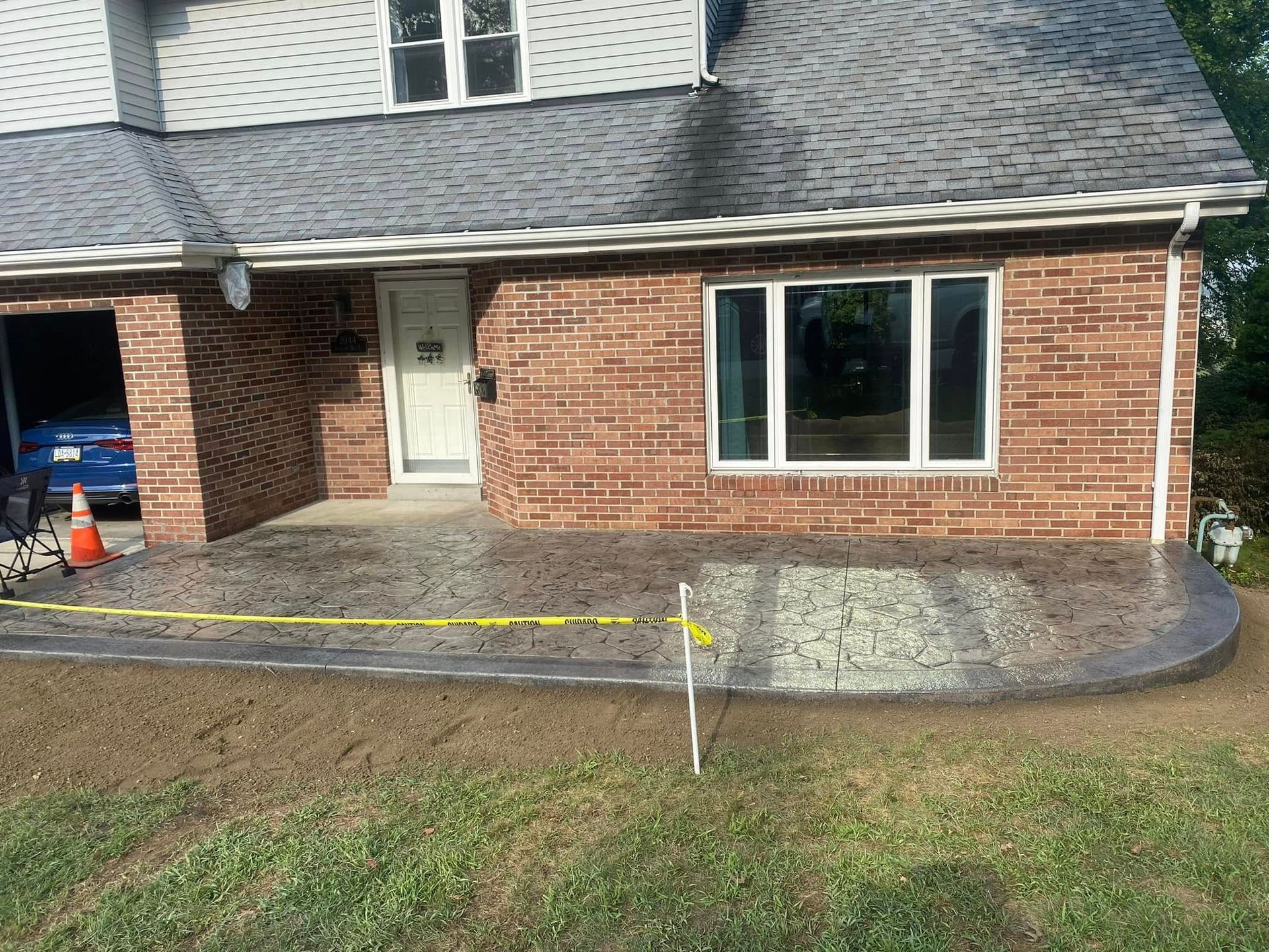 Brick house front with a new concrete walkway, yellow caution tape, and a cone by the porch