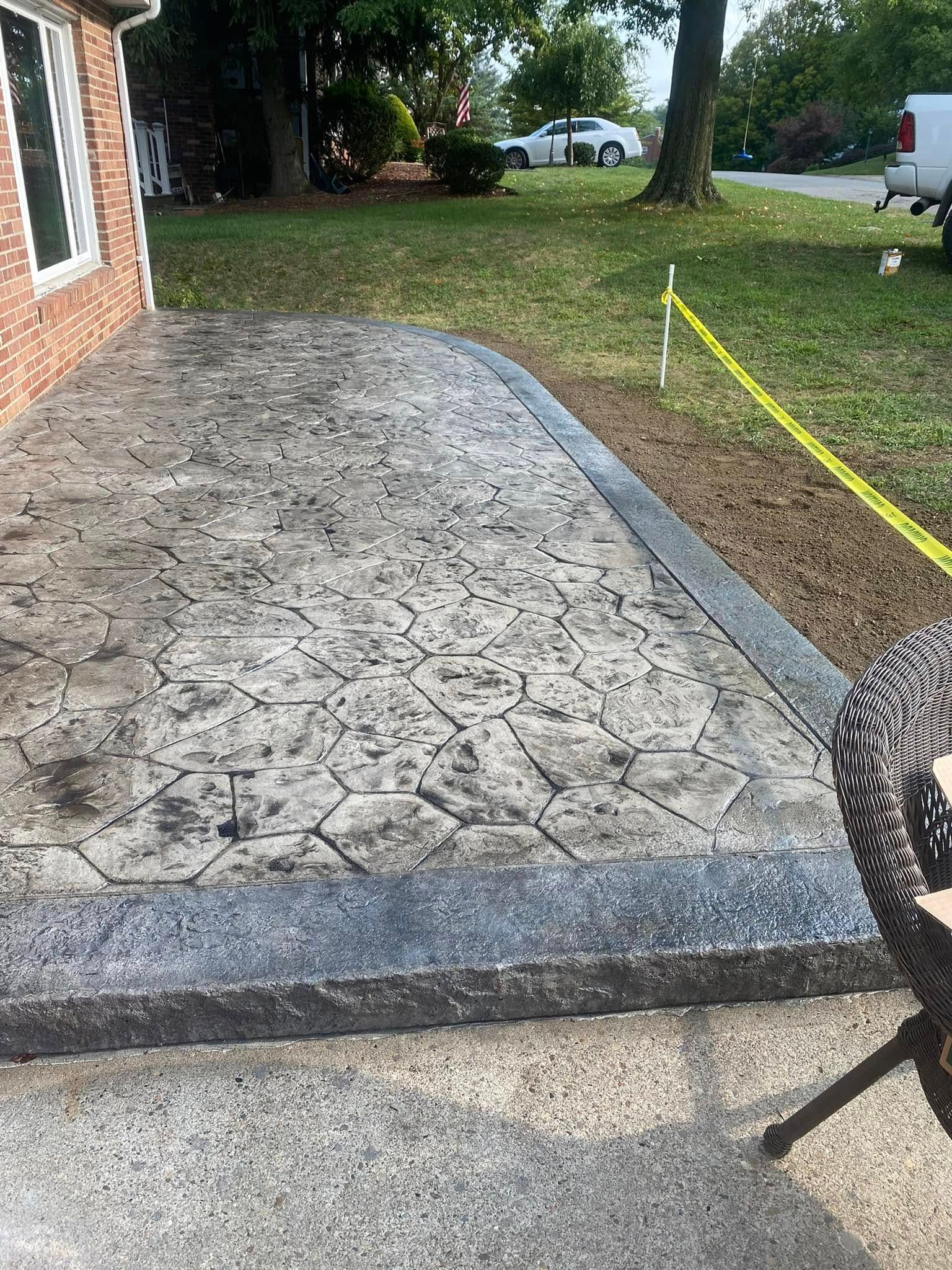 Stamped concrete driveway beside a brick house, bordered by grass and yellow caution tape.