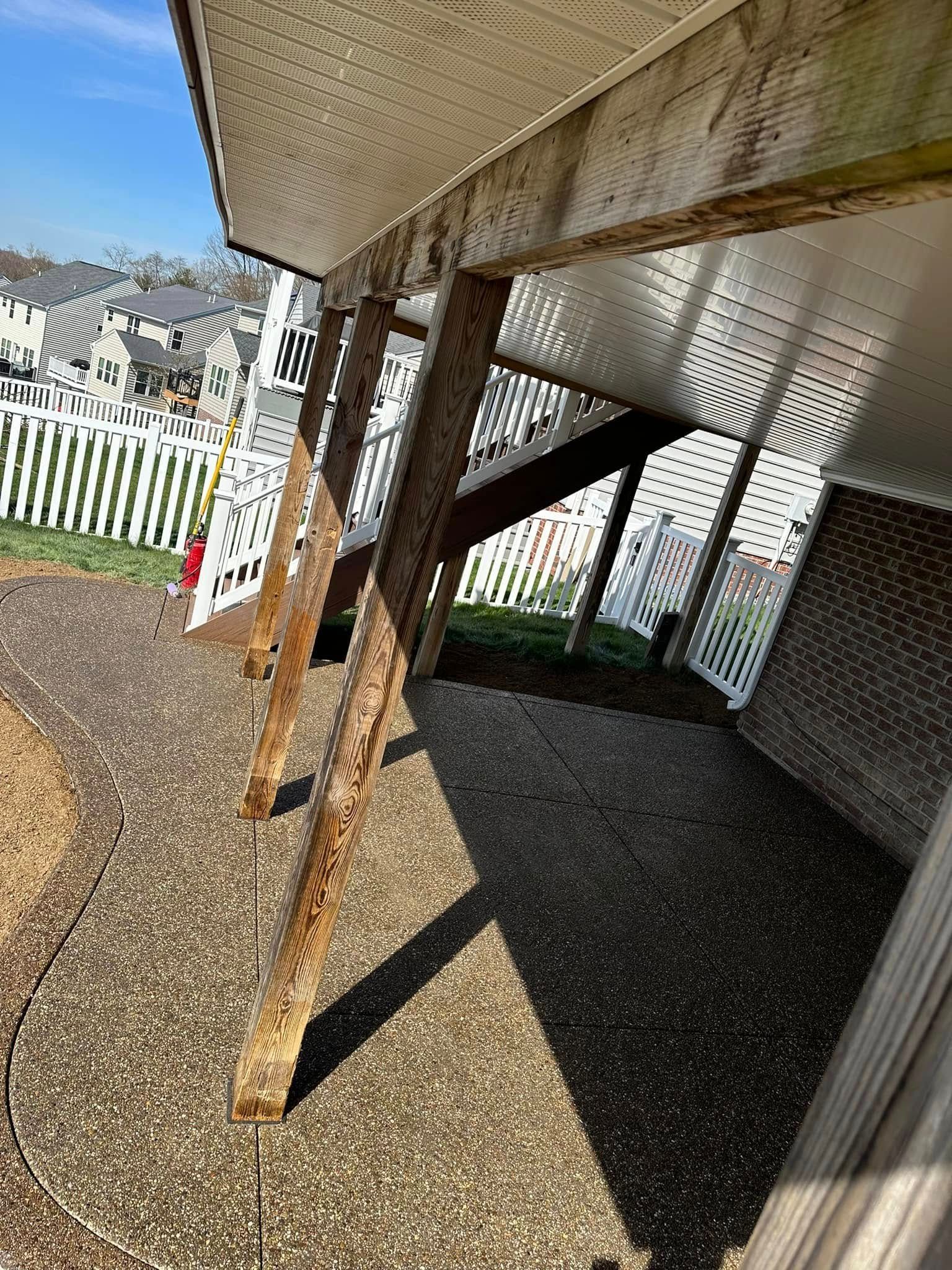 Rusty metal support posts under a covered porch beside a white fence and gravel yard.
