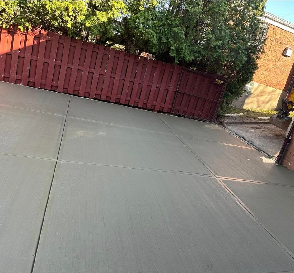 Tilted view of a concrete patio beside a red wooden fence and green bushes