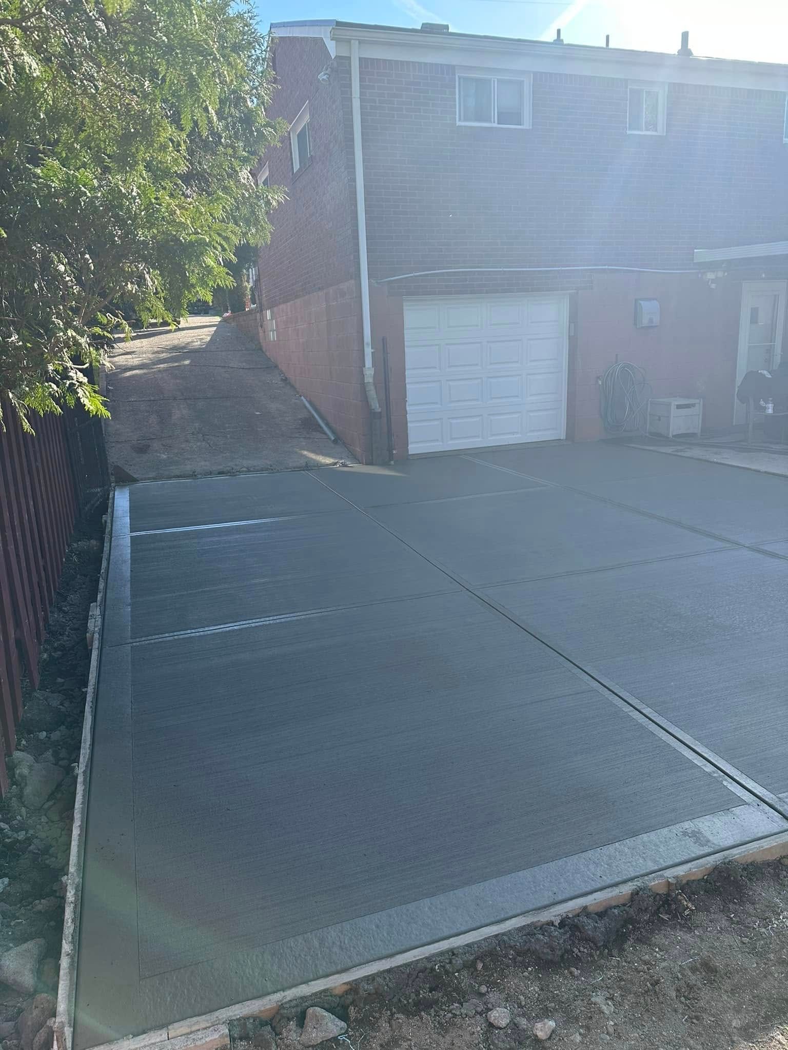 Residential driveway beside brick garage, with a concrete retaining wall and trees along the left side.