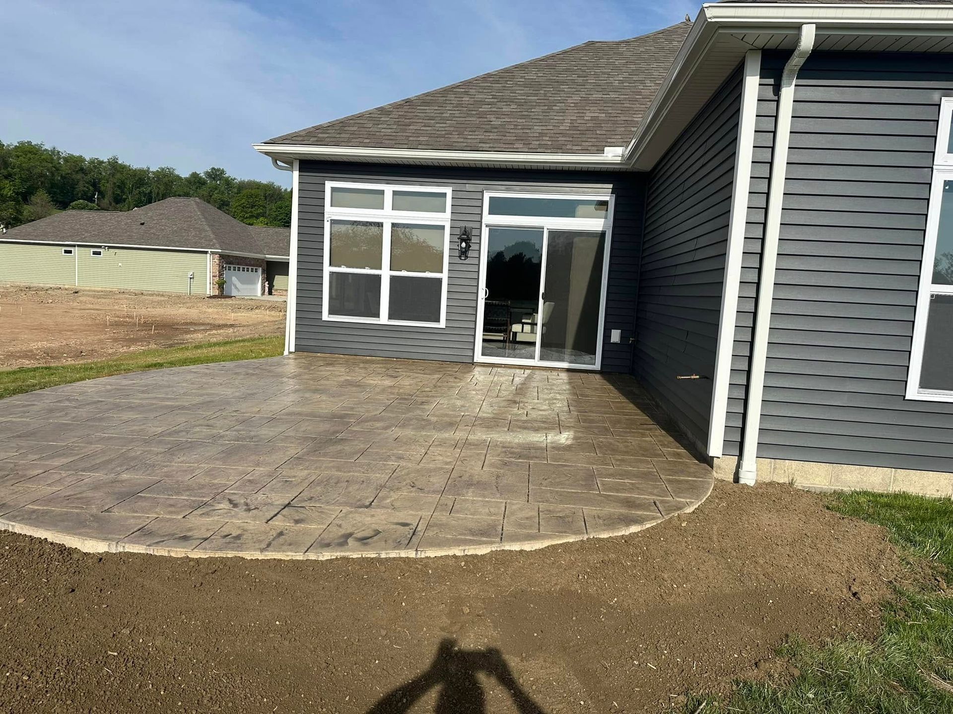Backyard patio with stone pavers beside a gray house and glass doors.