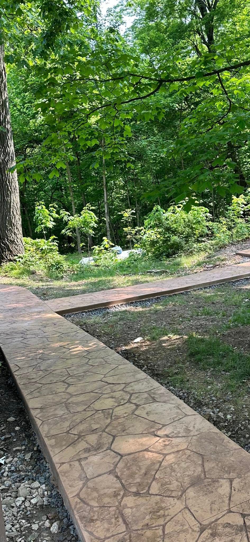 Stone walkway through a green wooded park with a path curving into trees and sunlight.