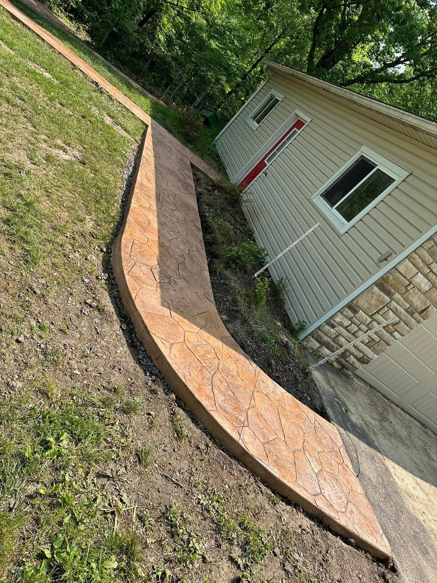 Curved brick garden border beside a house, with grass and a stone wall in the background.