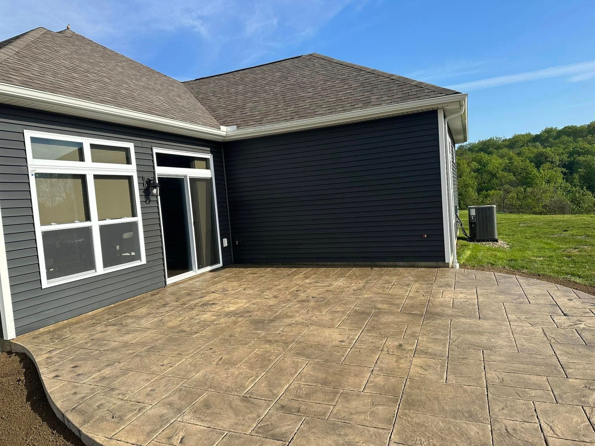 Back patio with stamped concrete, gray house wall, and black covered structure under a blue sky