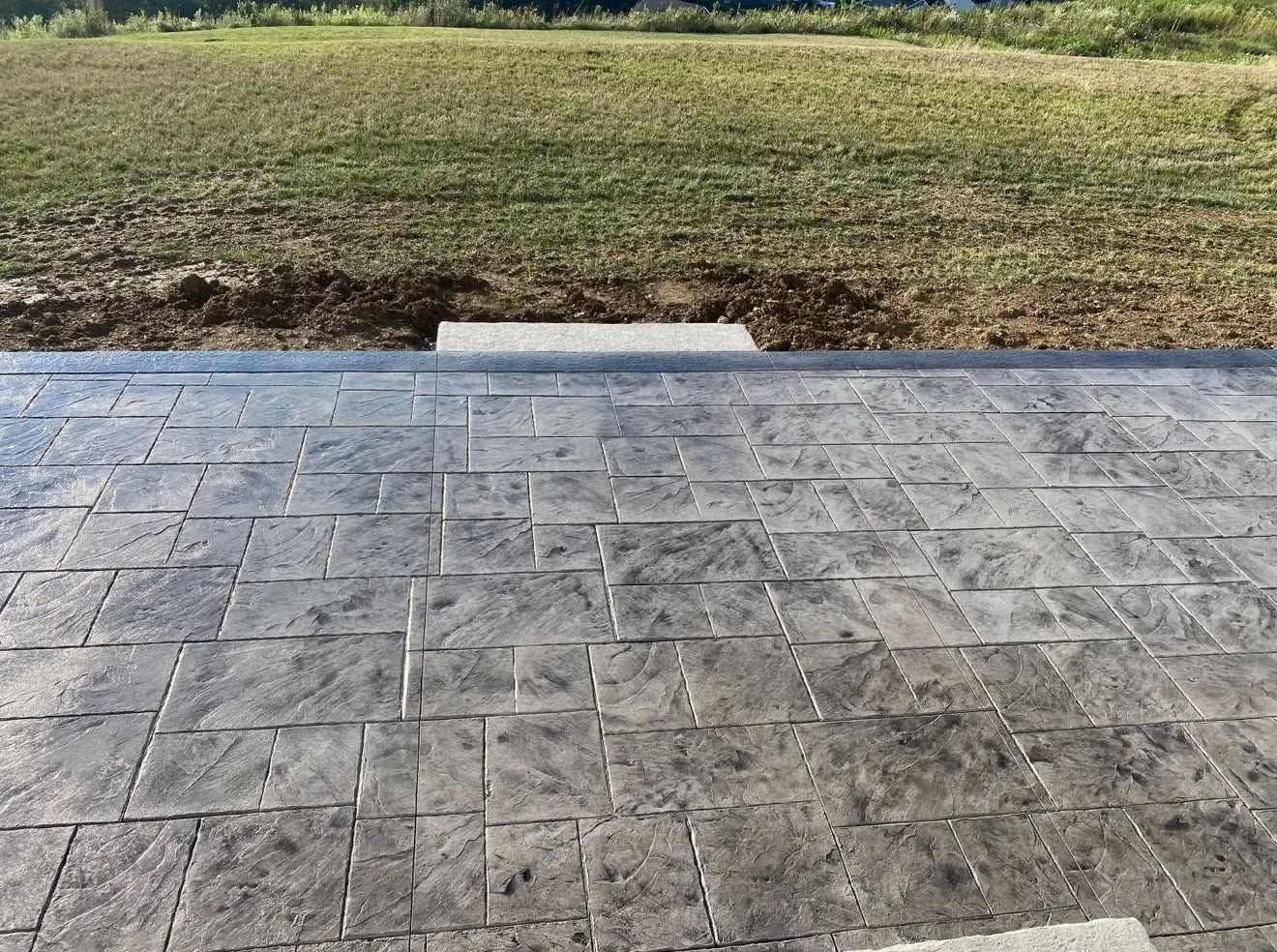 Stamped concrete patio beside a grassy yard with a small step in the center