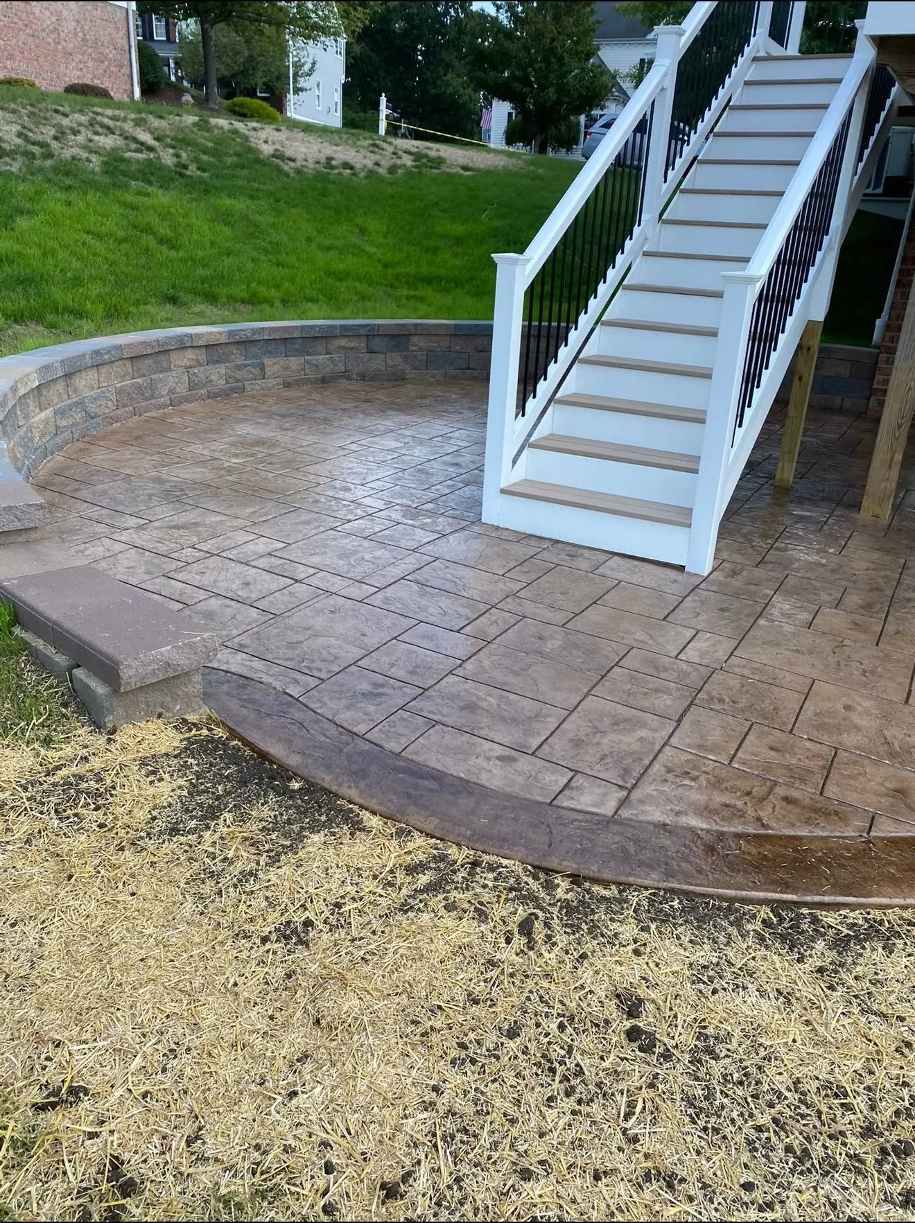 Stone patio with curved retaining wall and white outdoor staircase on a grassy slope