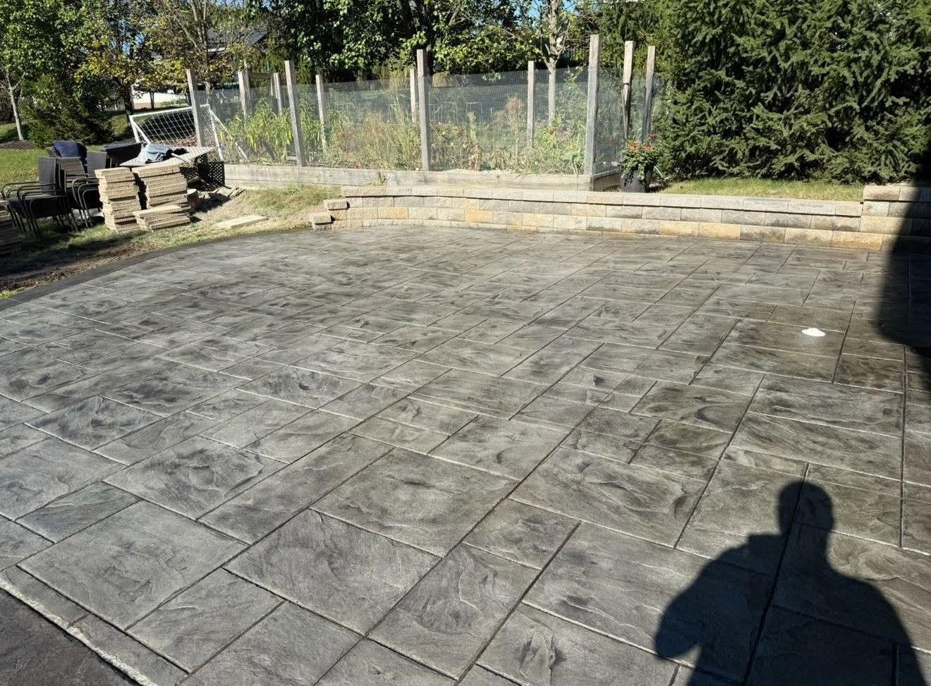 Empty stone patio with a low wall, fence, and trees in the background, viewed in bright sunlight