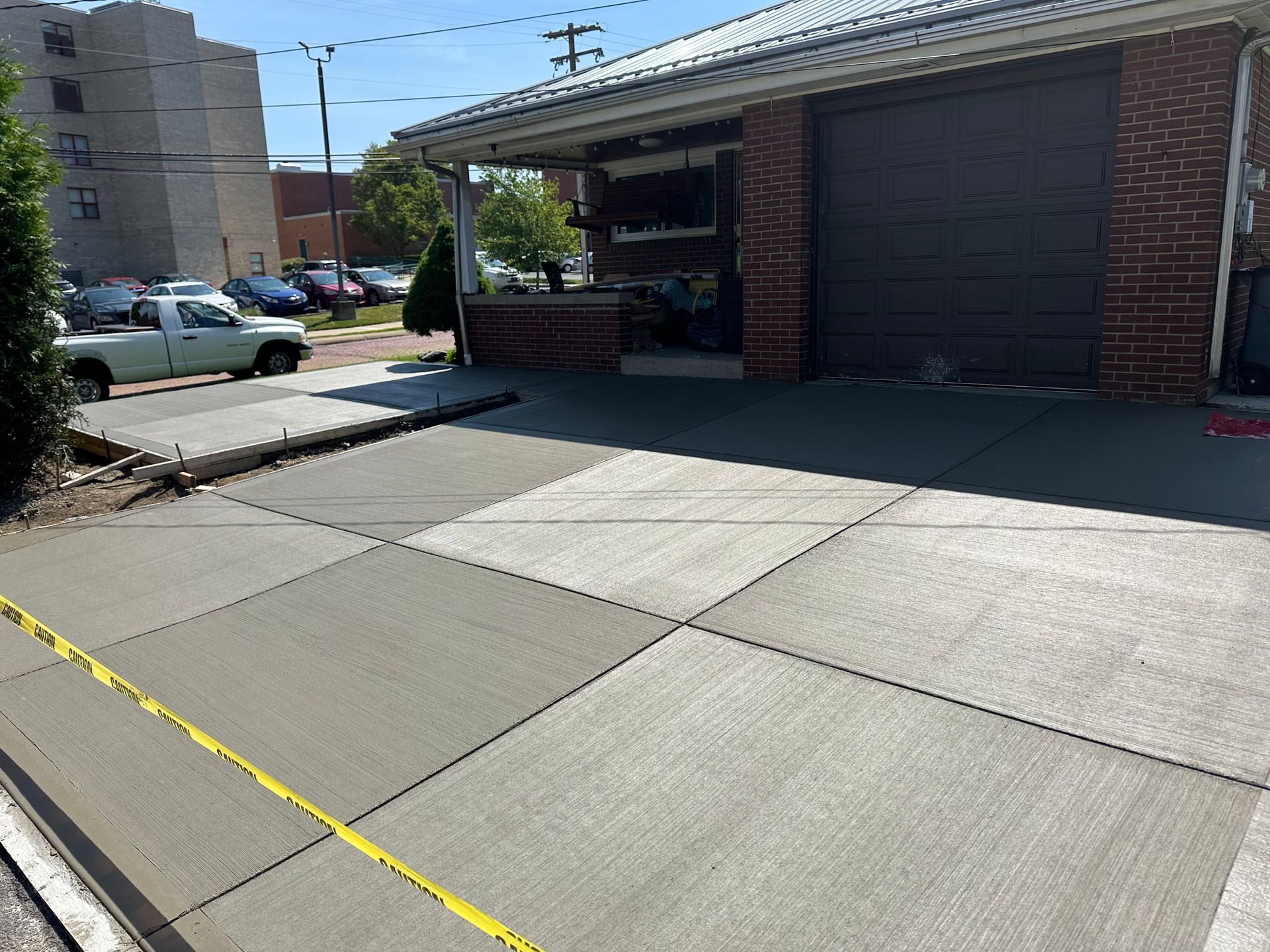 Concrete sidewalk and driveway beside a brick building with a garage door and parking area.