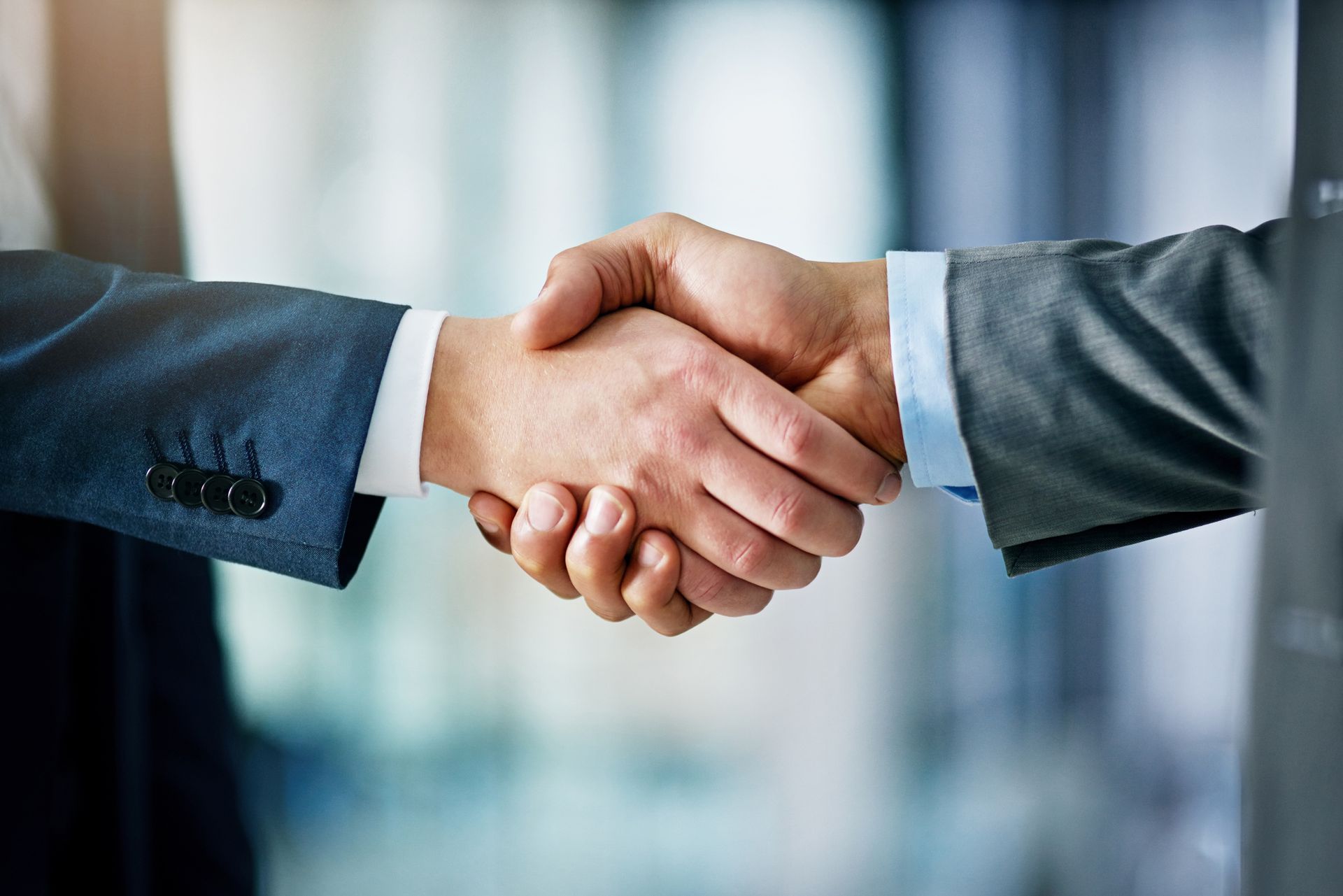 Two people in formal business suits shaking hands in an office setting.
