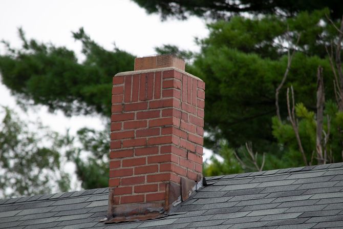 A brick chimney on top of a roof with trees in the background.