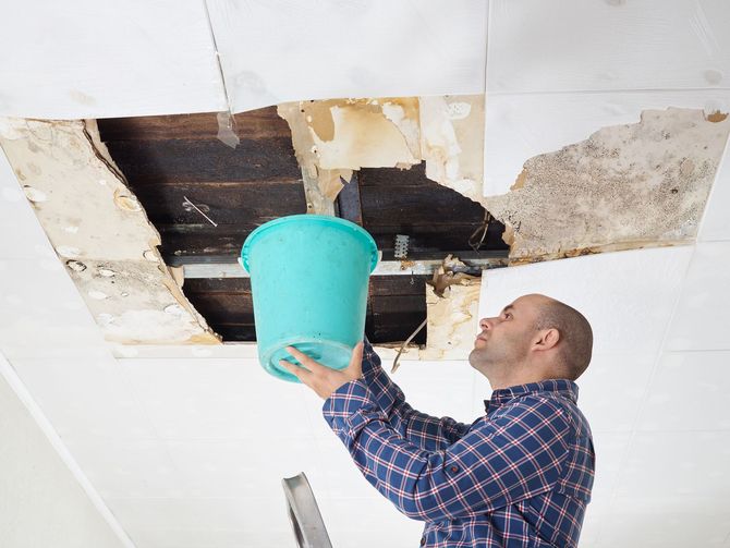A man is holding a bucket over a hole in the ceiling.