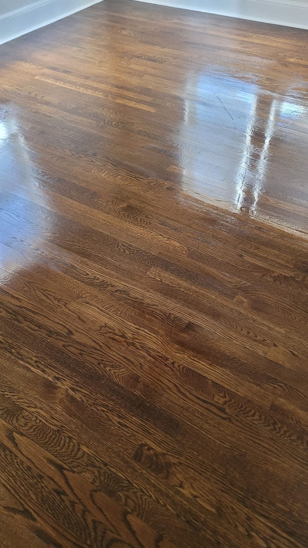 Glossy, dark stained hardwood floor reflecting light, with a white wall visible.