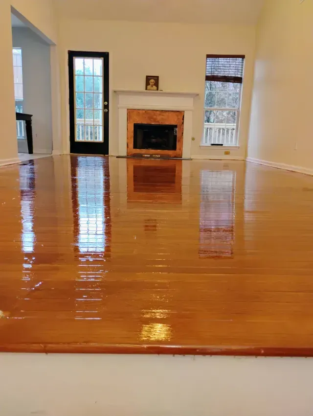 Newly refinished, glossy wooden floor in a living room; reflection of fireplace and windows.