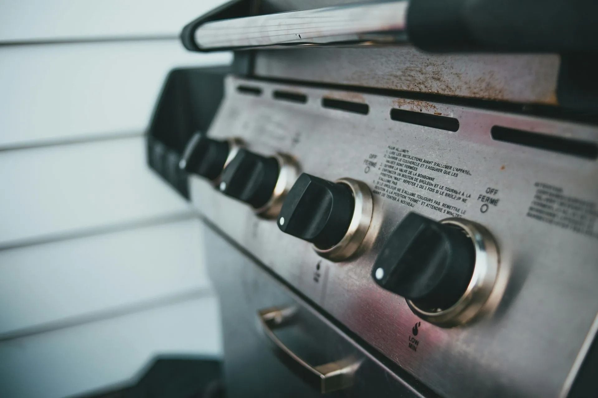 Close-up of a stainless steel gas grill with black control knobs and a side shelf