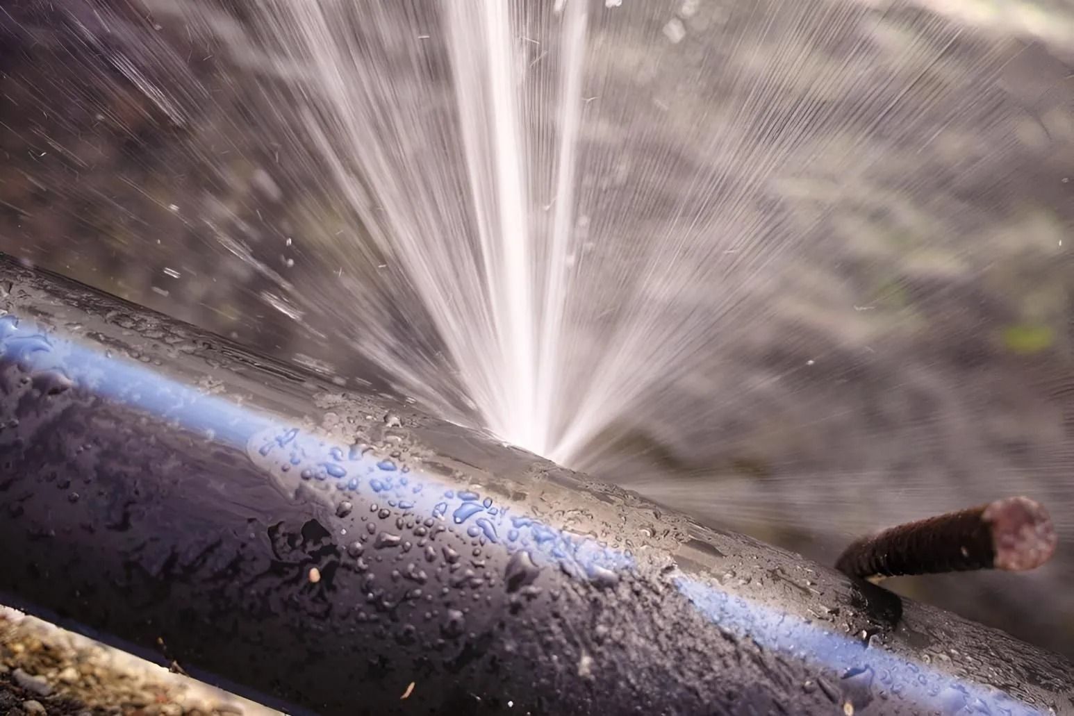 Water spraying from a broken pipe onto a wet metal surface outdoors