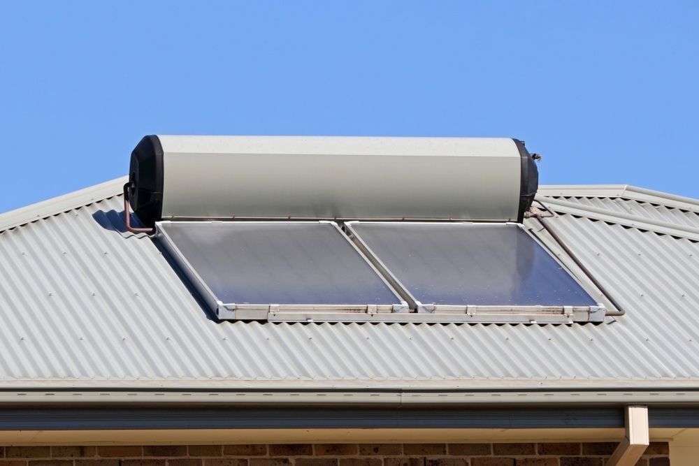 Solar water heater with two panels on a corrugated metal roof under a blue sky