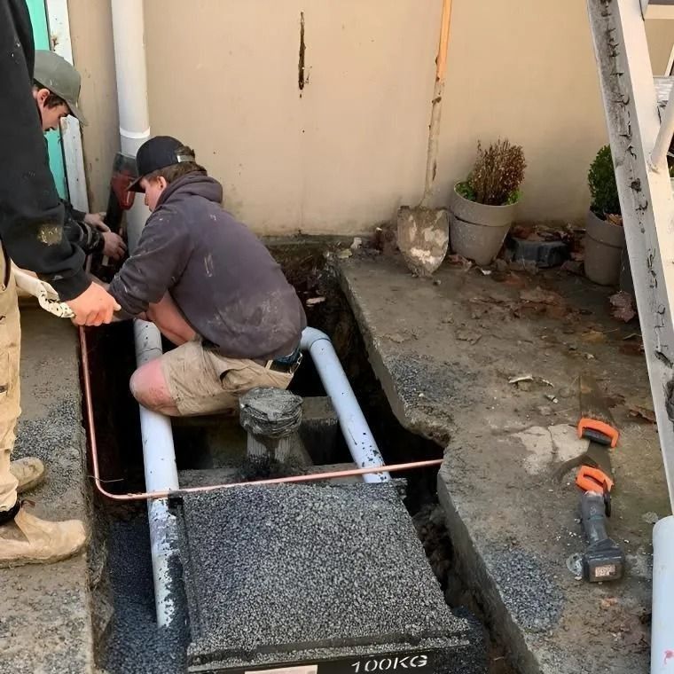 Workers installing a black hatch cover over a basement opening beside a wall