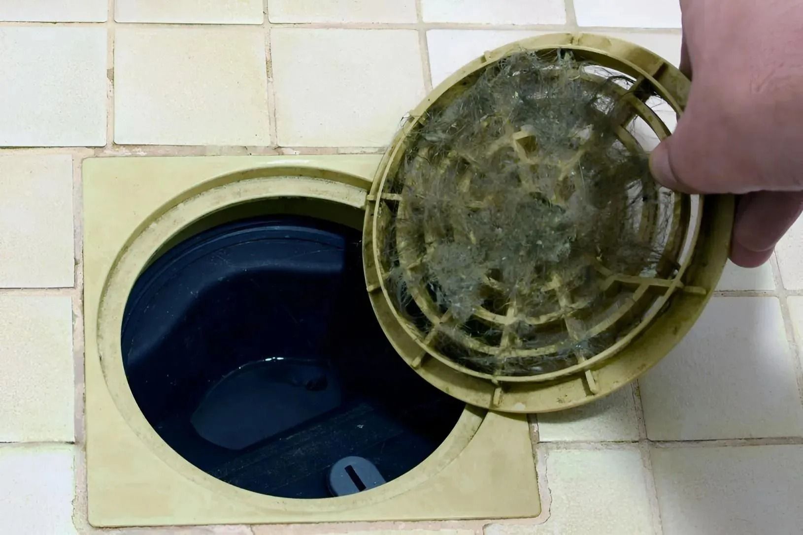 Hand lifting a round drain cover over a floor drain in tiled flooring
