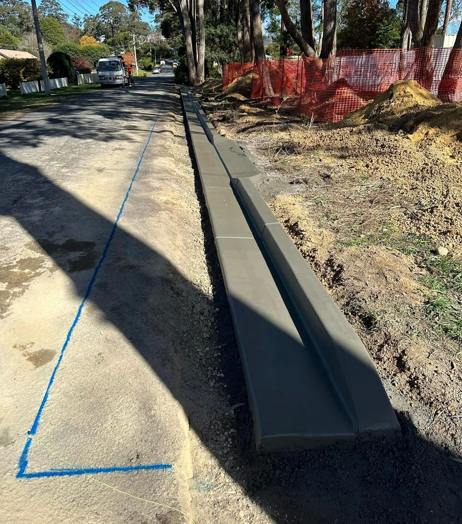 New concrete curb along a roadside ditch beside an orange construction fence