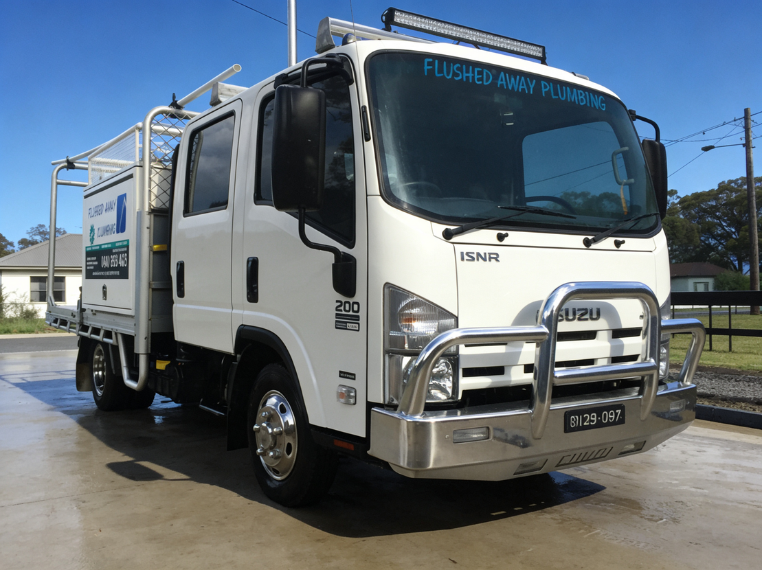 White Isuzu dump truck parked outdoors on a sunny day, facing left.