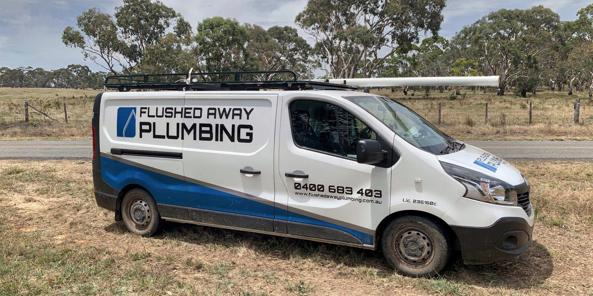White plumbing service van parked on dirt, labeled “Flushed Away Plumbing,” with blue stripe and ladder on top