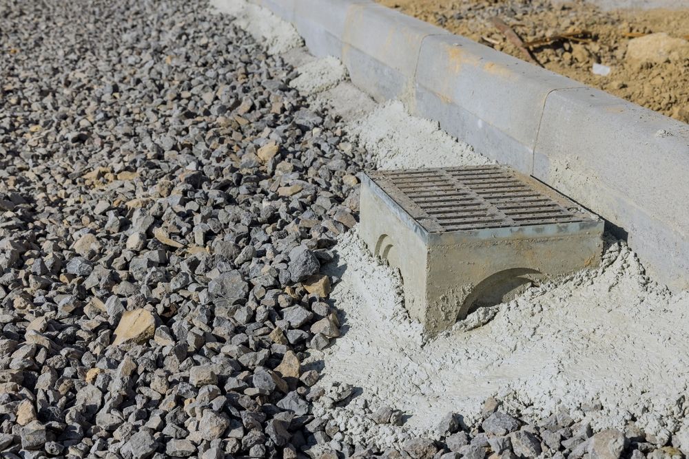 Concrete drainage culvert beside gravel along a sloped roadside embankment