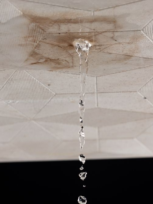 Water dripping from a ceiling hole onto a patterned surface, with a dark area below.