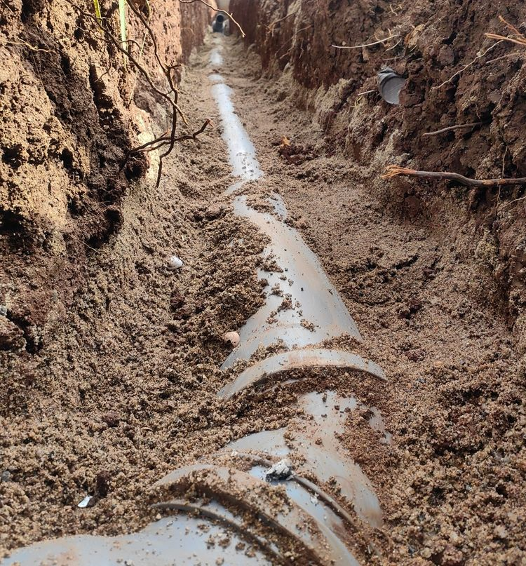 Partially buried white pipe in a muddy trench with standing water