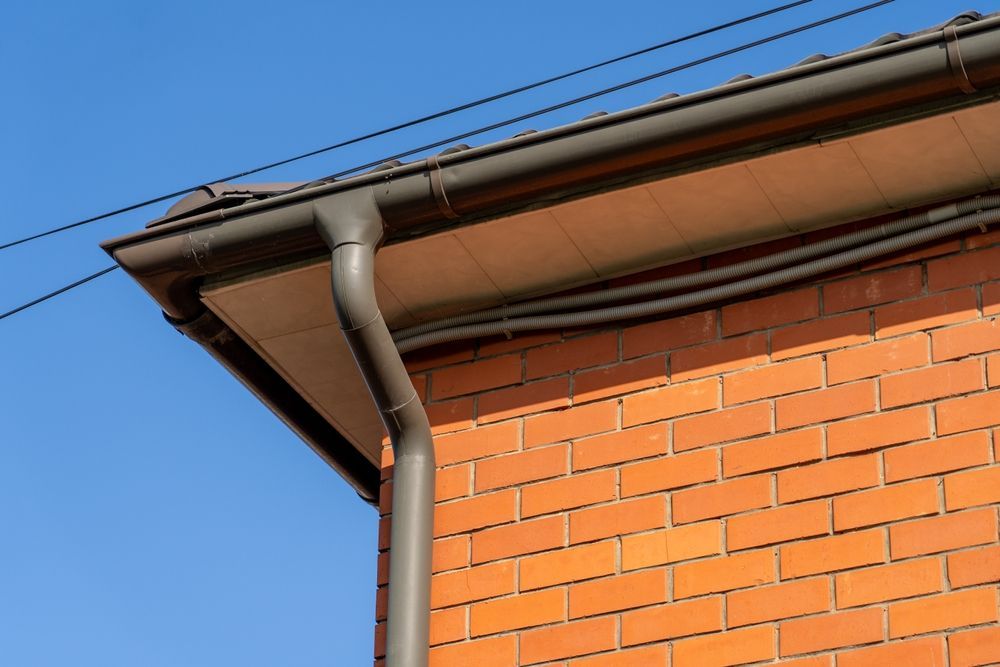 Brick house corner with gray gutter and downspout against a blue sky